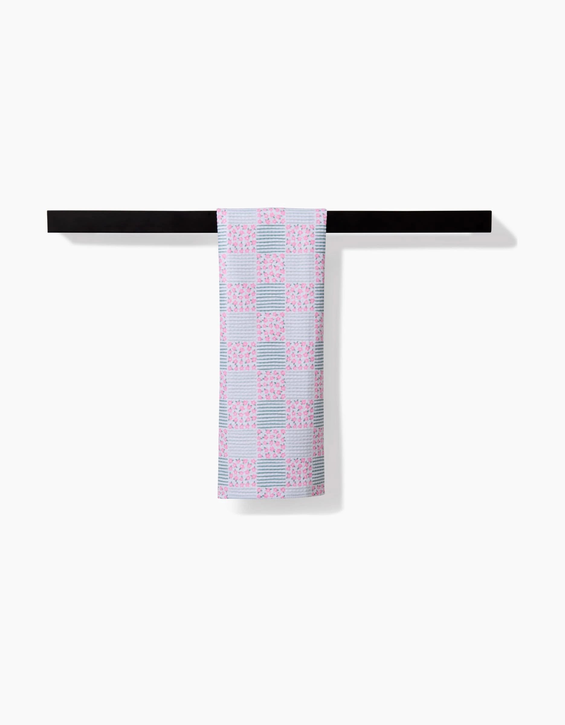 A Hufton Studio Mini Flowers and Stripes Check Pink and Green bar towel hangs neatly over a simple, horizontal black bar on a white background.