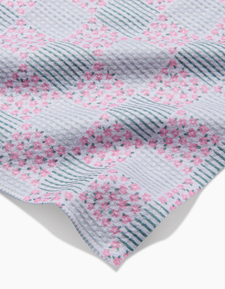 A close-up of Hufton Studio’s Mini Flowers and Stripes Check Pink and Green Bar Towel, crafted from Geoweave fabric, showing blue stripes and clusters of pink flowers on a white background, with a soft, textured look.