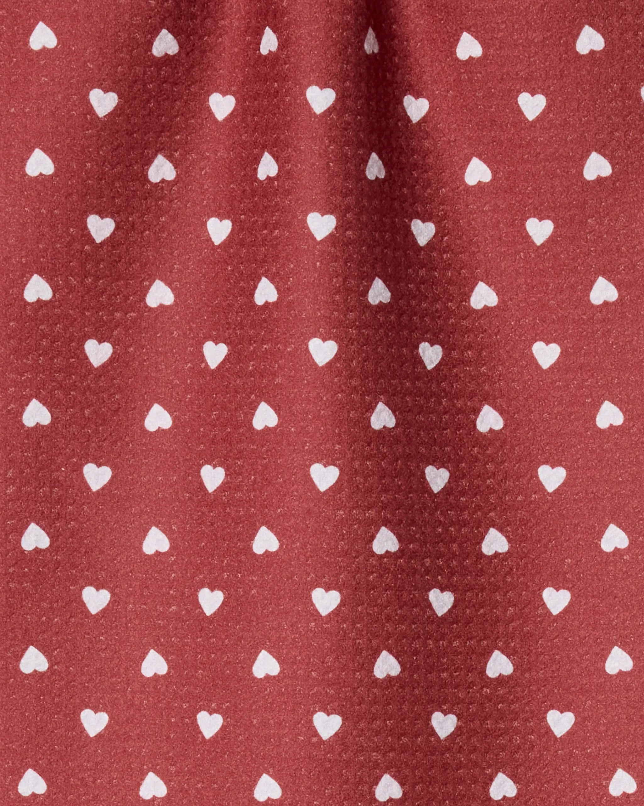 Geometry’s Mini Heart bar towel showcases a repeating small white heart pattern on textured red fabric with visible folds. Made from recycled materials, it combines eco-friendly appeal and charming design.