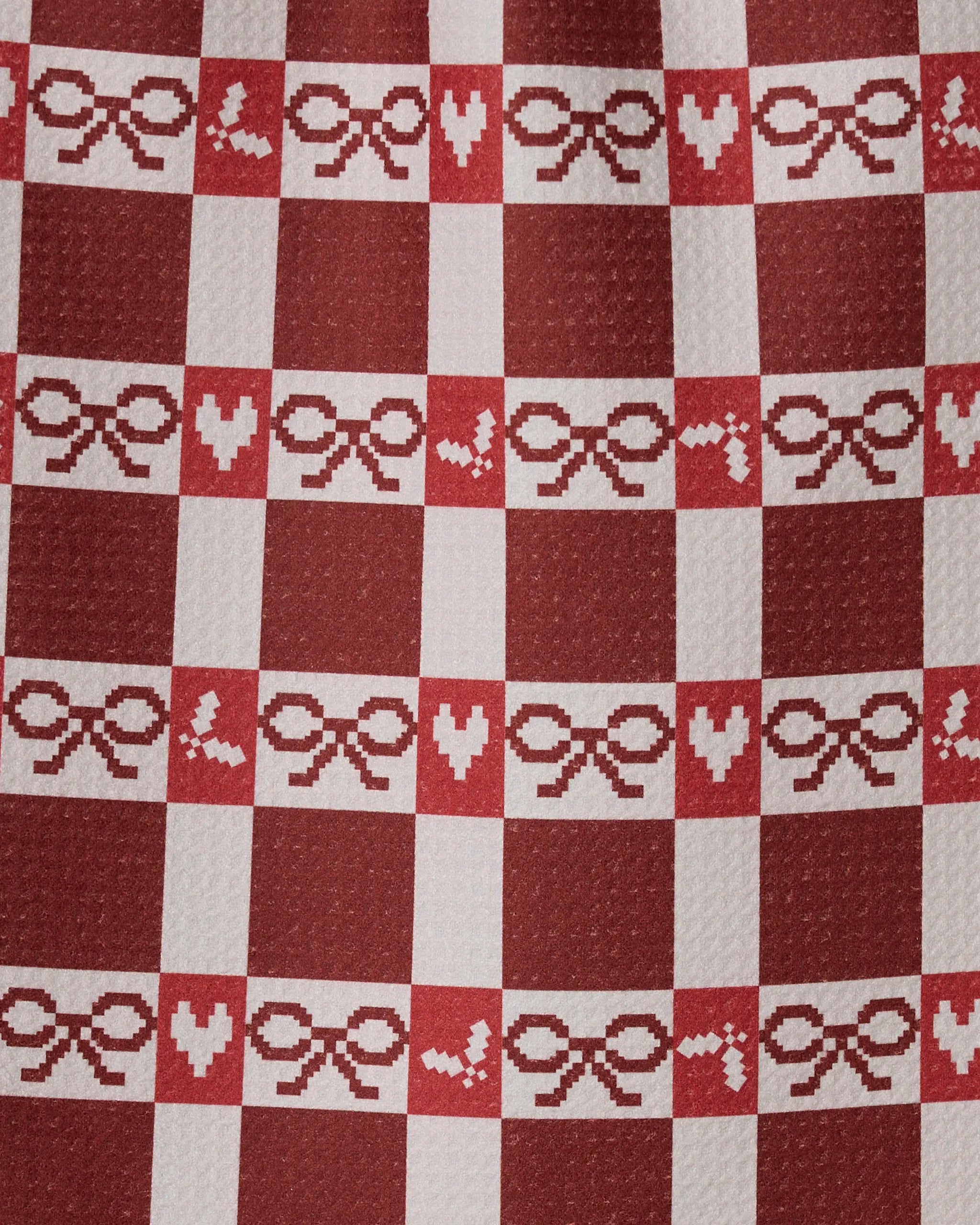 The Mistletoe Gingham bar towel by Geometry features red and white checks with pixelated hearts, bows, and birds—made from recycled materials for charm and sustainability.