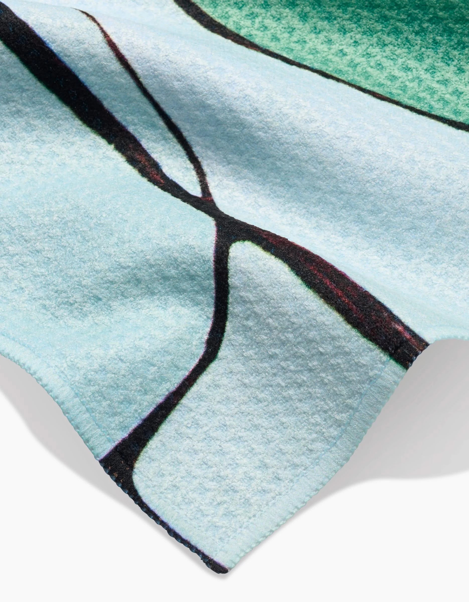 A close-up of the Modern Poppy bar towel by Rachel Austin shows its textured Geoweave fabric, with dark abstract lines, a green section, and detailed edges on the light blue material.