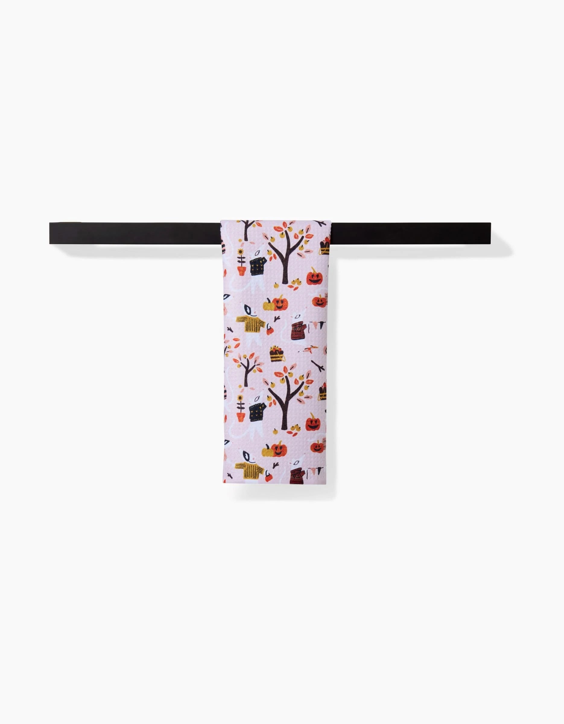 The Morticia bar towel by Amy MacCready, featuring pumpkins, trees, leaves, and houses in autumn colors, is draped over a black towel bar set against a plain white background.