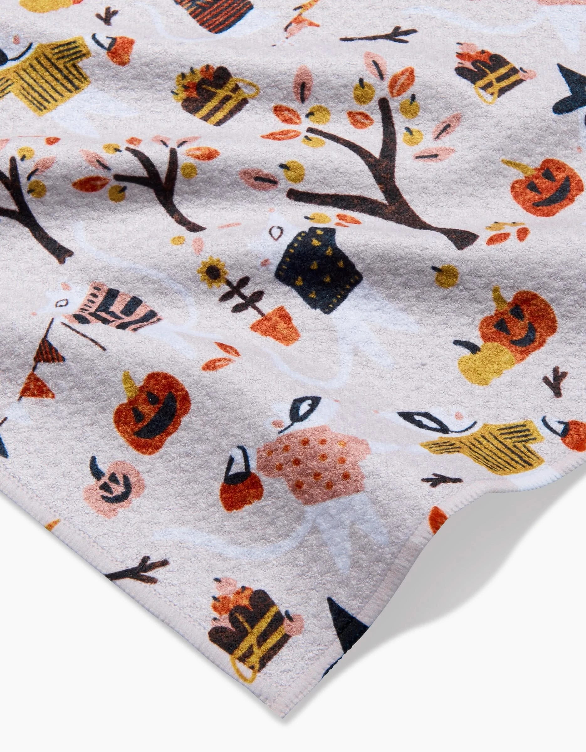 The Morticia kitchen towel by Amy MacCready features a fall-themed pattern with pumpkins, autumn trees, pies, hats, brooms, and mugs on a light background. Made from recycled material; fabric appears slightly wrinkled in some areas.