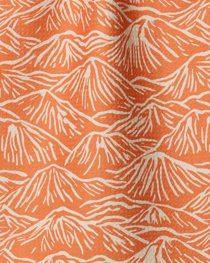 The Geometry Mountain Range towel features Geoweave fabric with an orange background and a repeating pattern of stylized, white outlined mountain shapes for a textured, wavy look.