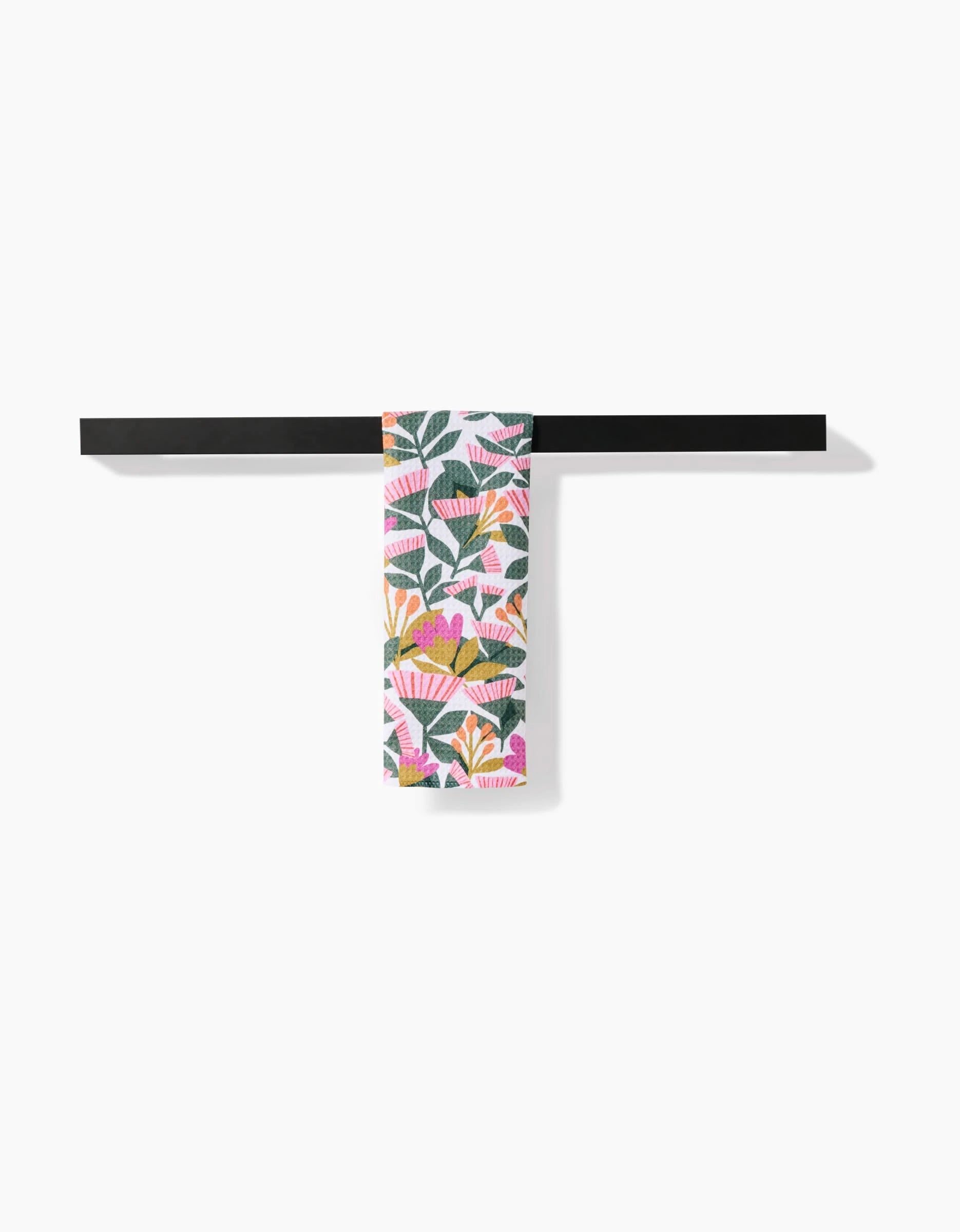 The Lisa Nelson Moxie Mauve bar towel, featuring a vibrant floral pattern on Geoweave fabric, hangs on a sleek black towel bar against a plain white background.