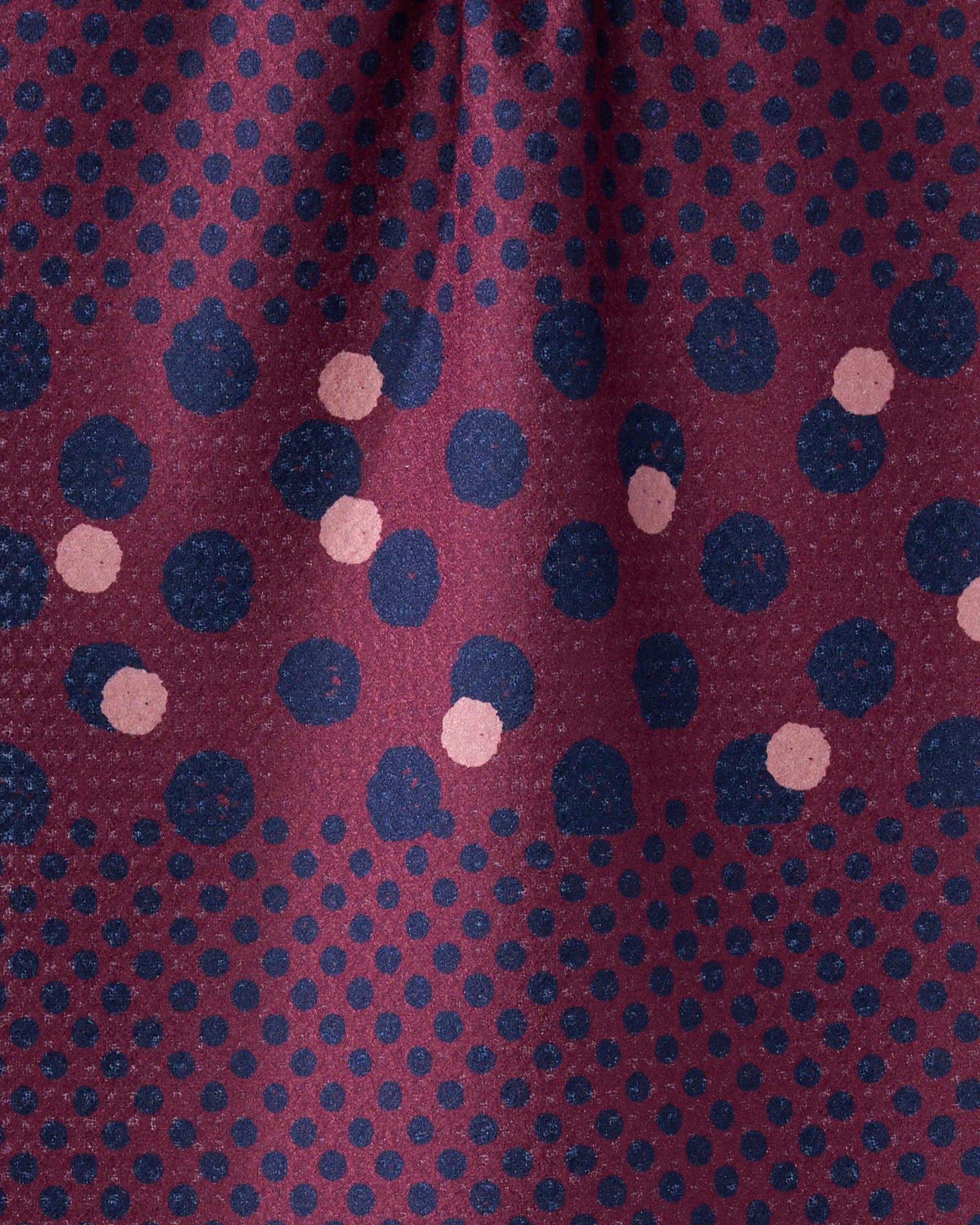 A close-up of Geometry's Mulberry Dot fabric, crafted from recycled materials, showcases evenly spaced dark blue dots with light pink accents in a subtle zigzag on maroon.
