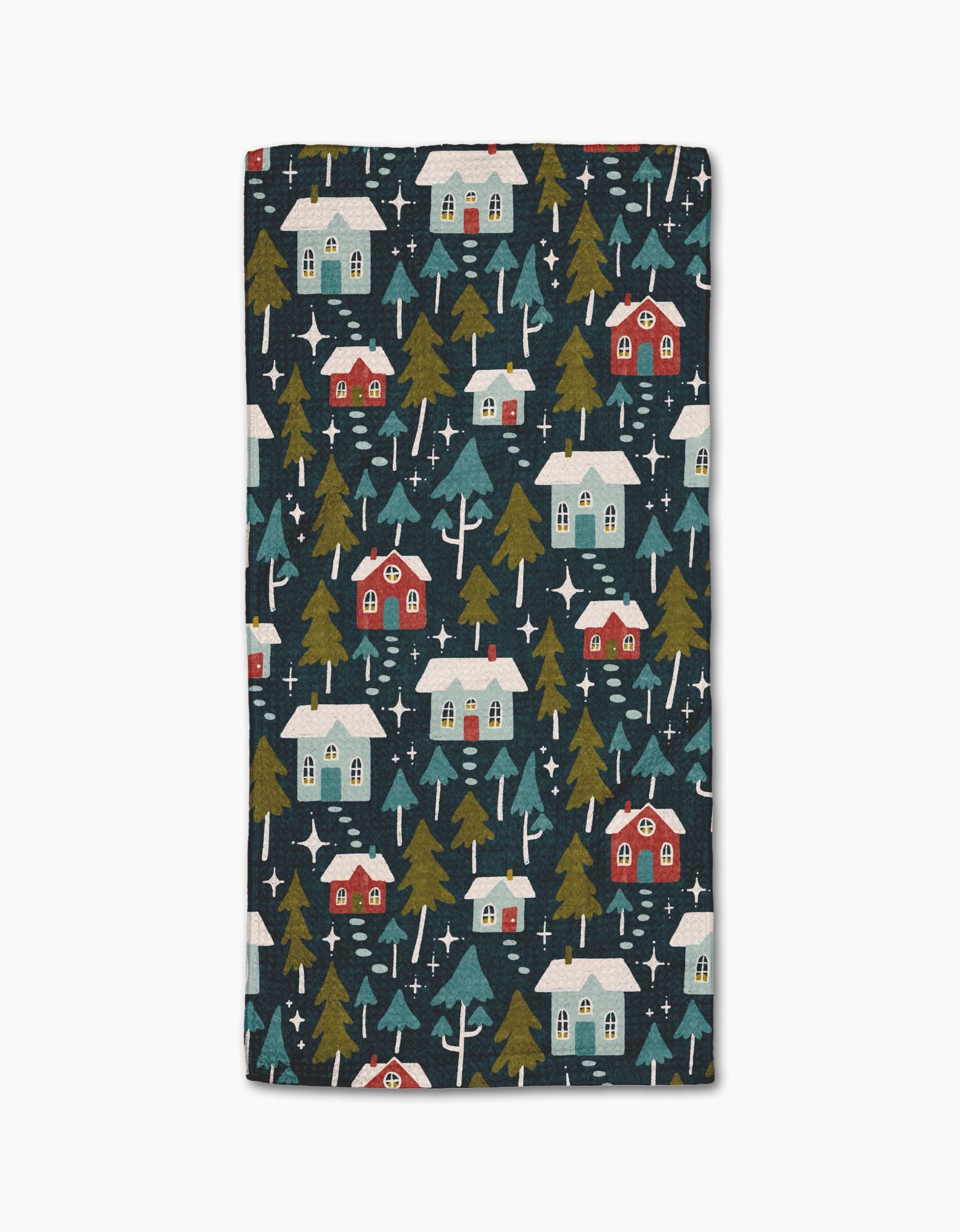 The Nico Dark towel by Amy MacCready is a rectangular bar towel made from recycled materials, showcasing a festive winter design with red and blue houses, snowy roofs, green pines, and white stars on a dark background.