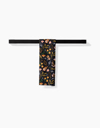 The Megan Roy Nighttime Botanical black bar towel, featuring vibrant floral and mushroom designs on Geoweave fabric, hangs neatly folded over a simple black towel bar against a white background.