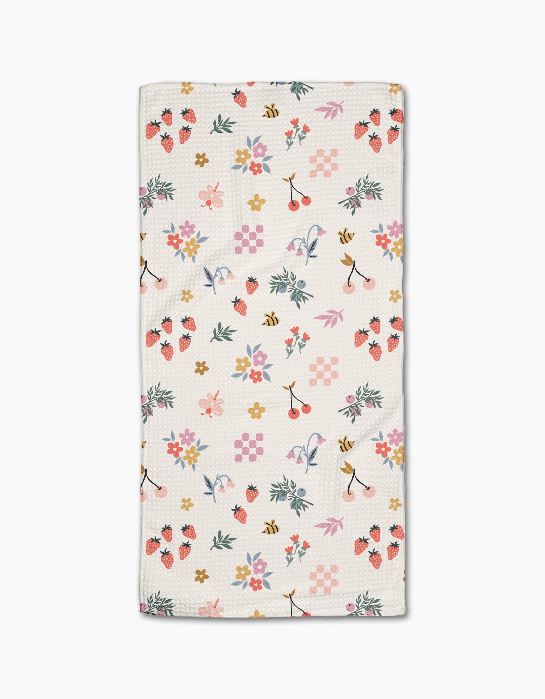 The North Meadow Morning Bar Towel by Charlie Rowan Designs features a colorful pattern of strawberries, cherries, bees, flowers, leaves, and shapes in pink, yellow, green, and purple on white—crafted from sustainable recycled materials.