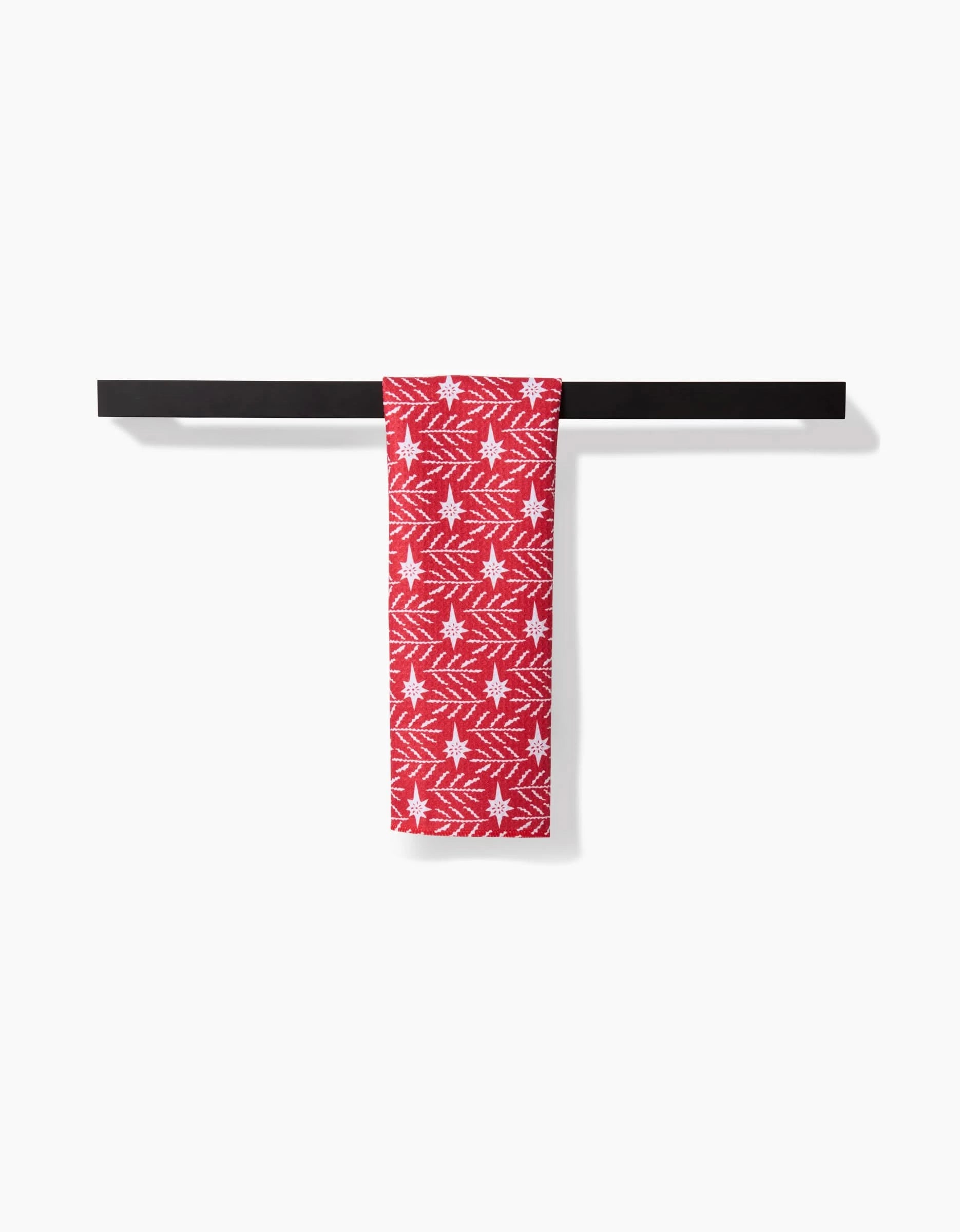 The Roxy Marj “North Star” towel, in red with a white Christmas star and branch pattern, hangs neatly on a black horizontal towel bar against a plain white background.