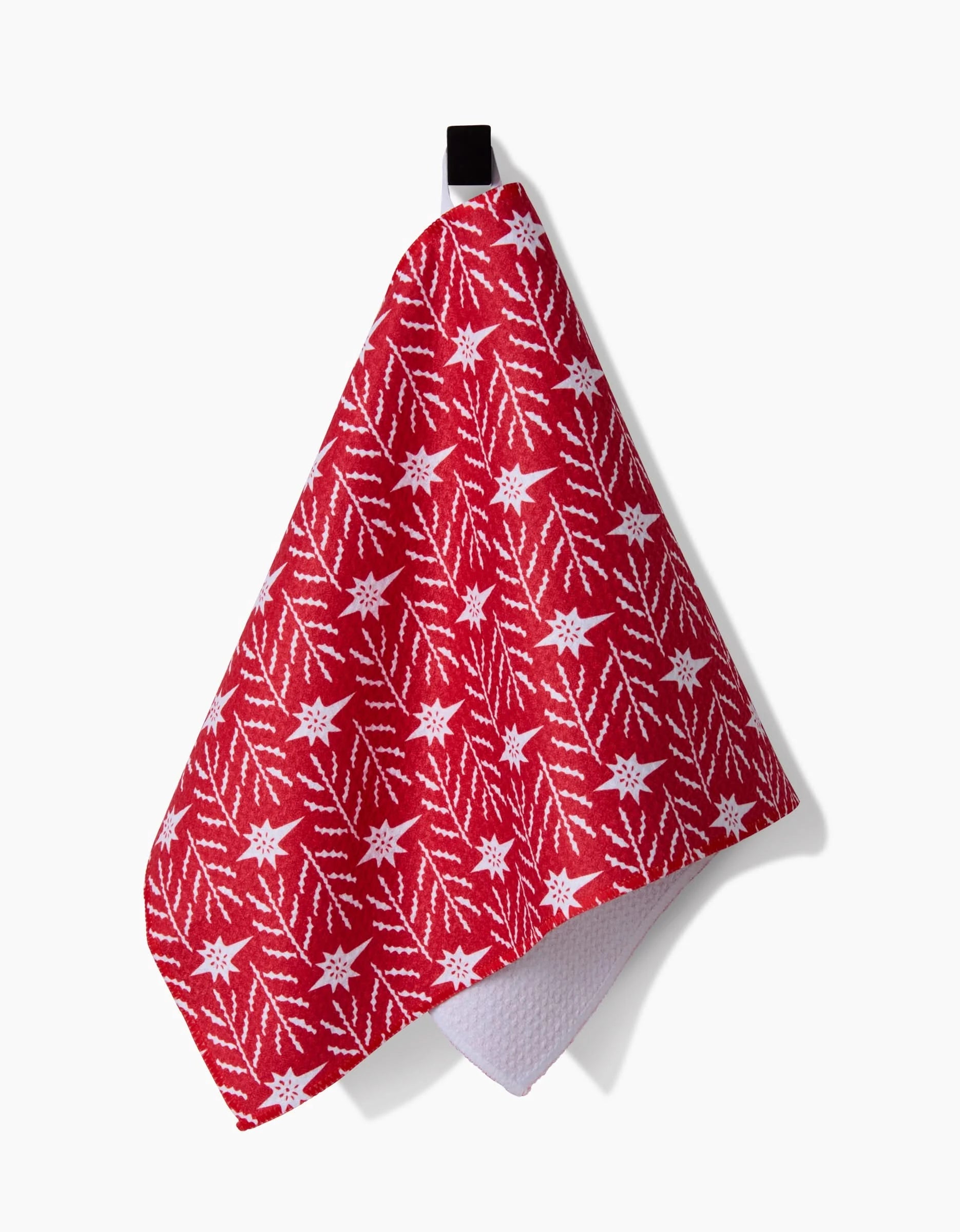The Roxy Marj North Star towel, featuring a white snowflake and branch design on red, hangs from a black loop against a plain white background.