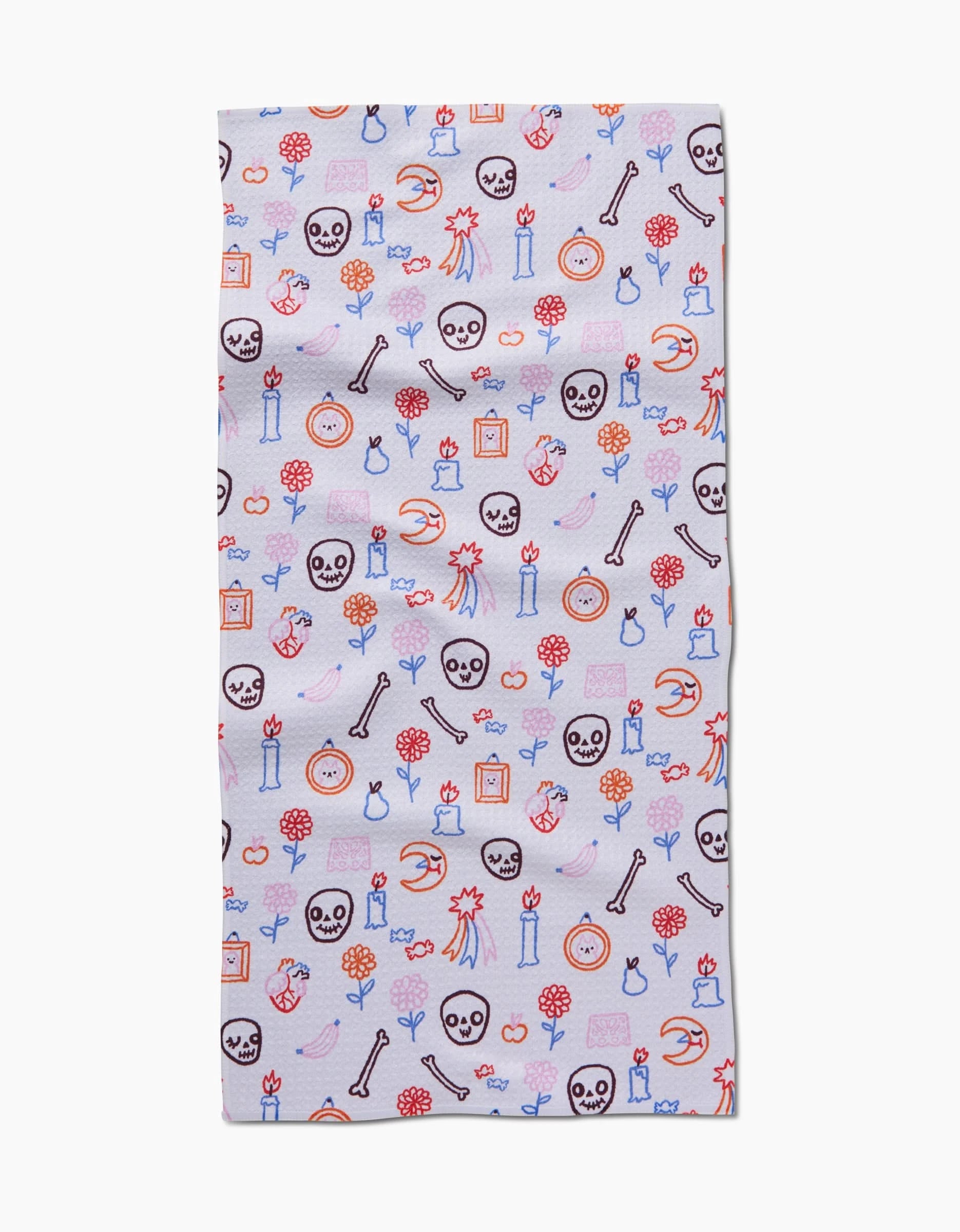 The Offerings Bar Towel by So Lazo features Geoweave fabric and whimsical Halloween illustrations—skulls, bones, pumpkins, candles, flowers, and potions—in orange, blue, and black on a light background.