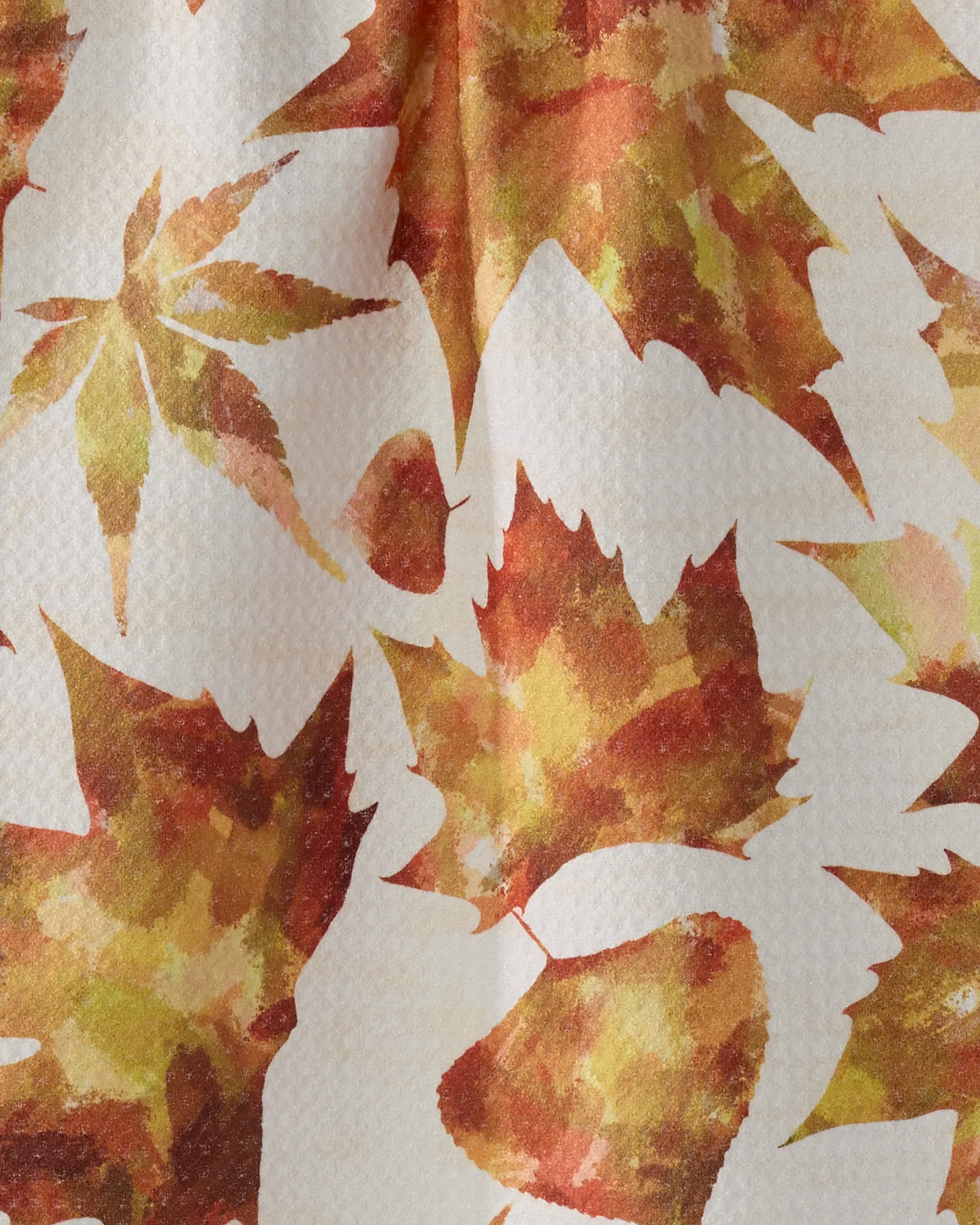 The Geometry "Painted Fall" bar towel is textured, made from recycled materials, and displays autumn leaves in orange, red, and yellow for a cozy seasonal touch.