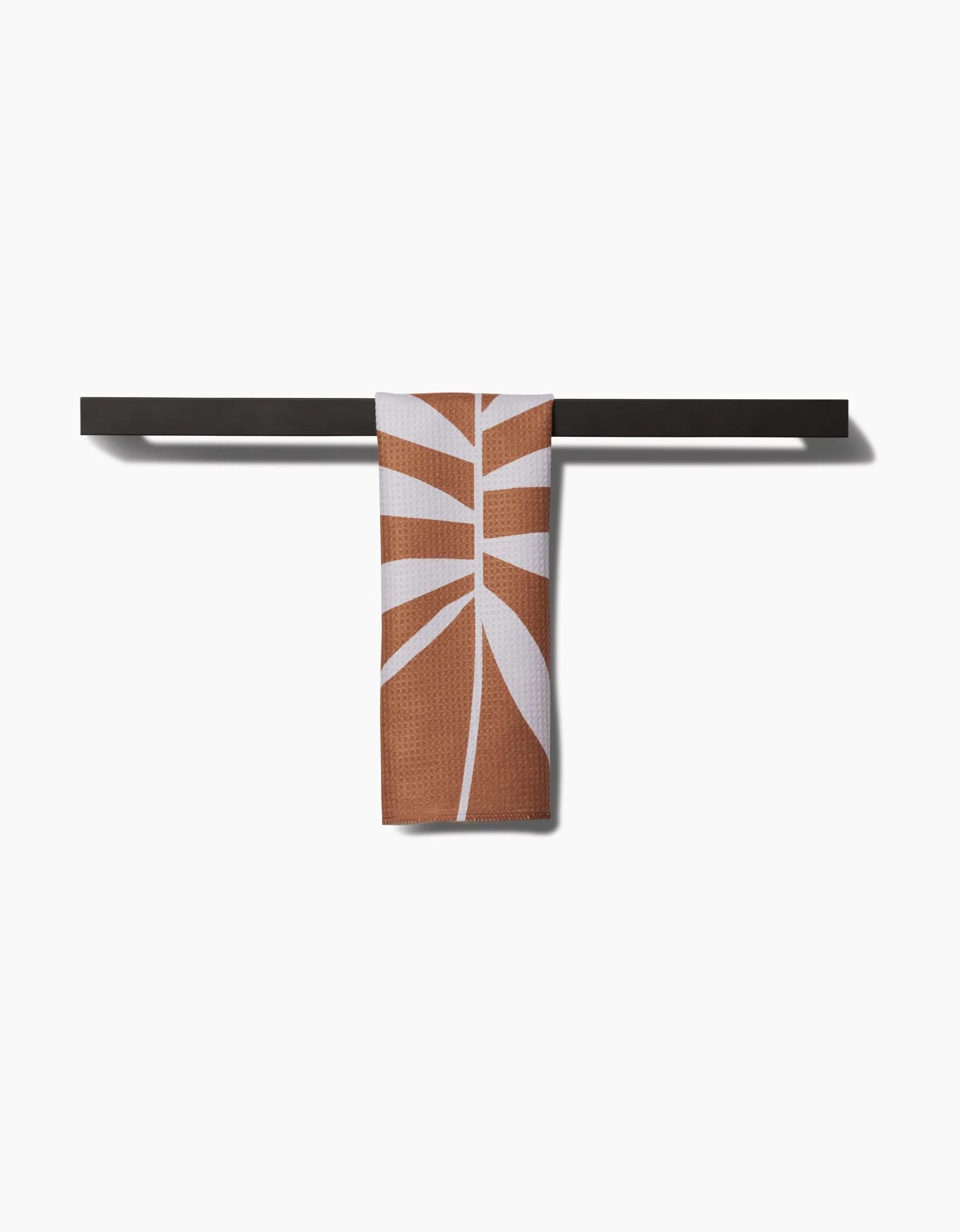 The PrintedPlant Palm bar towel, featuring a brown and white geometric leaf design on ultra-absorbent Geoweave fabric, hangs over a sleek black bar with a plain white background.
