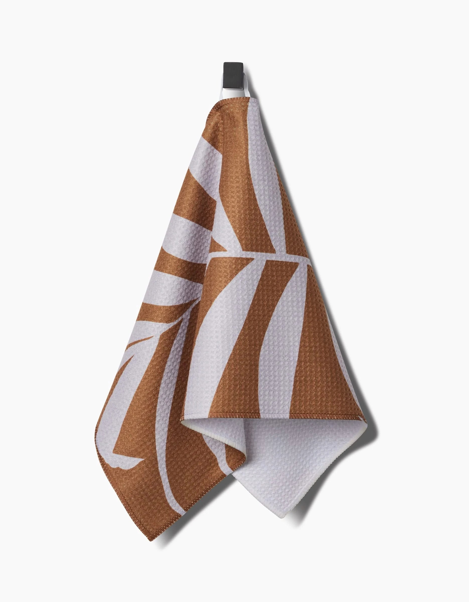 A PrintedPlant Palm brown and white patterned ultra-absorbent bar towel hangs from a black hook against a plain white background.