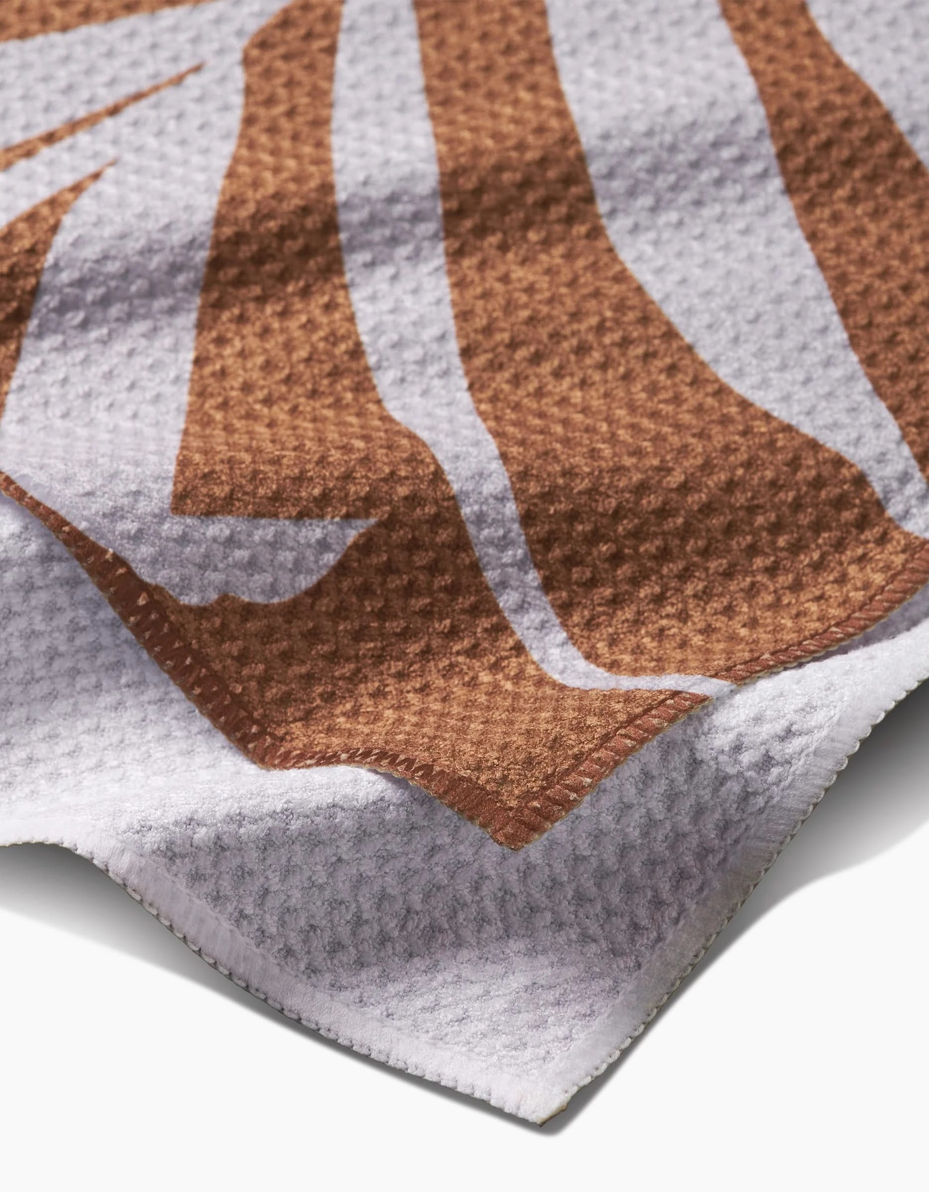 A close-up of the PrintedPlant Palm Bar Towel showcases its ultra-absorbent Geoweave fabric, brown and white abstract pattern, and detailed edge.