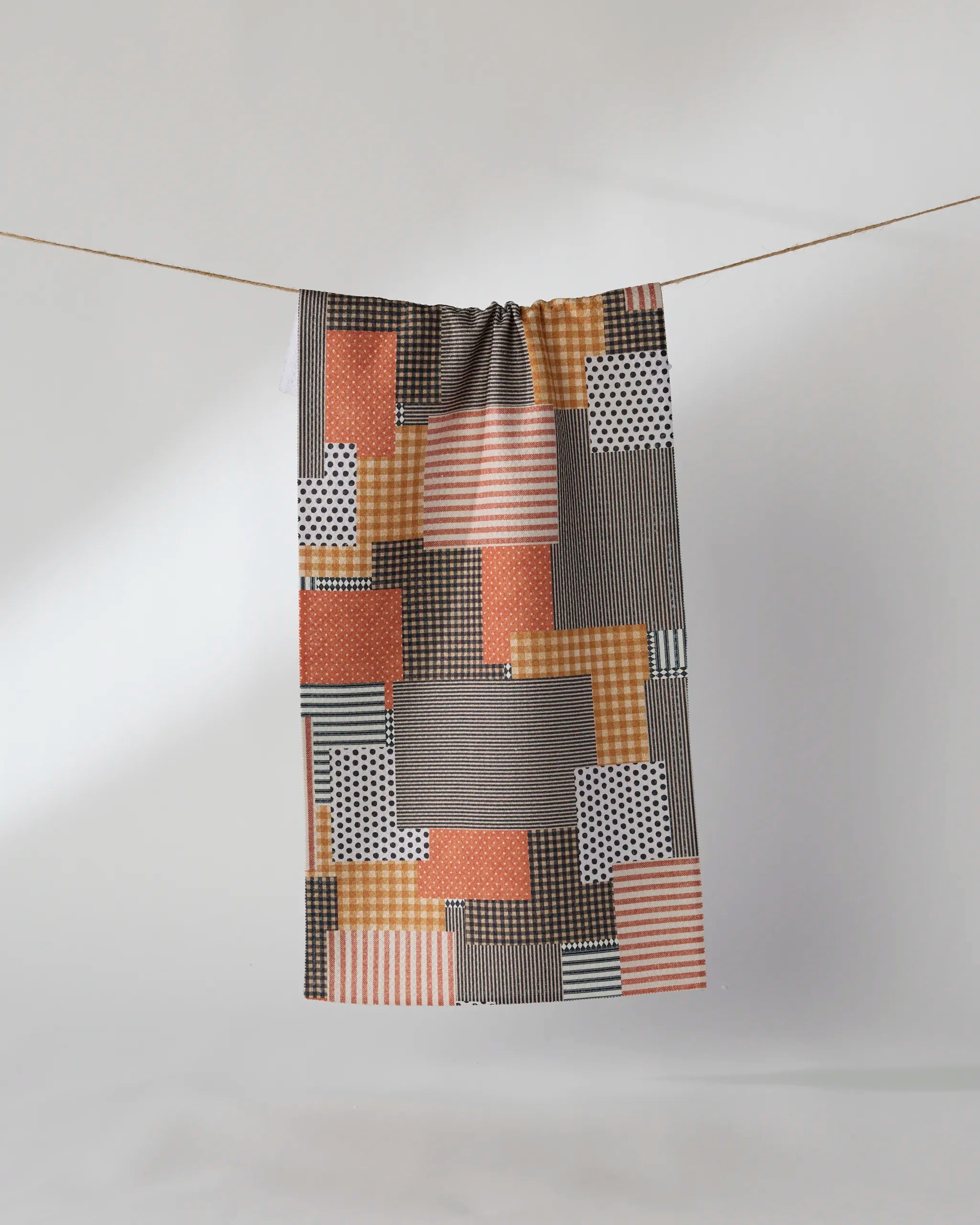 Patch and Pumpkin by Geometry features a rectangular Geoweave fabric with an orange, black, white, and beige patchwork of geometric prints, displayed on a clothesline against a plain light background.