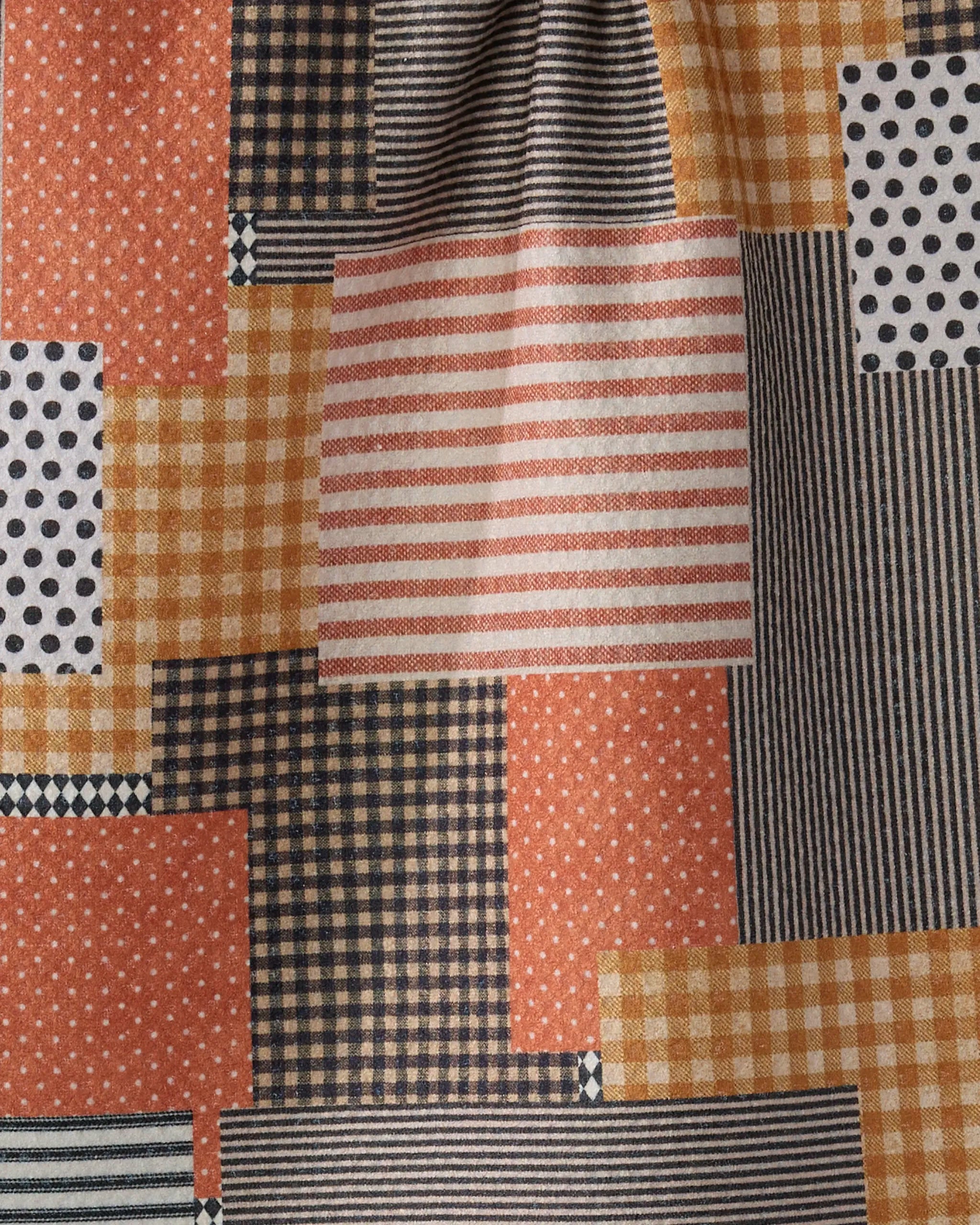 The Geometry Patch and Pumpkin towel features Geoweave fabric with a patchwork of rectangles in stripes, checks, polka dots, and stars in orange, black, white, and beige.