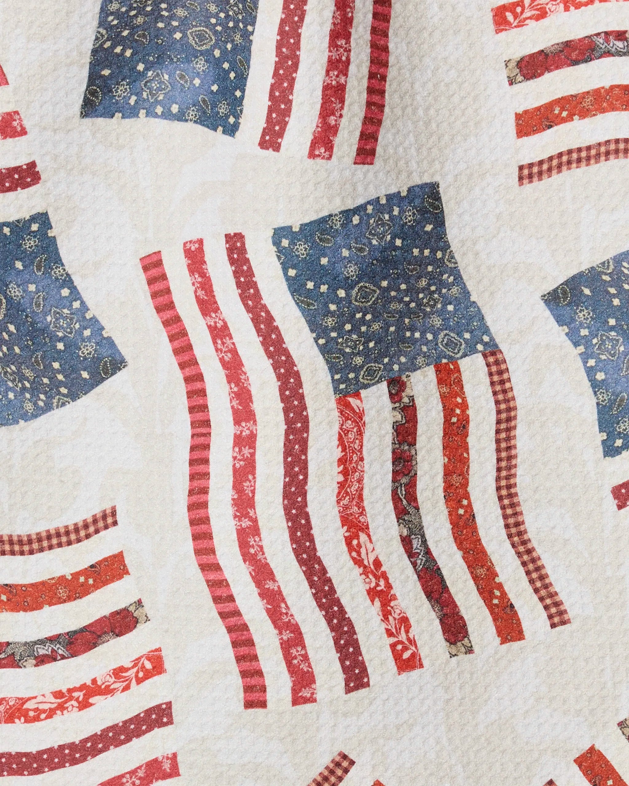 The Patchwork Pride towel by Geometry features a quilted, rustic American flag design in red, white, and blue on a cream background—ideal as a decorative bar towel for patriotic gatherings.