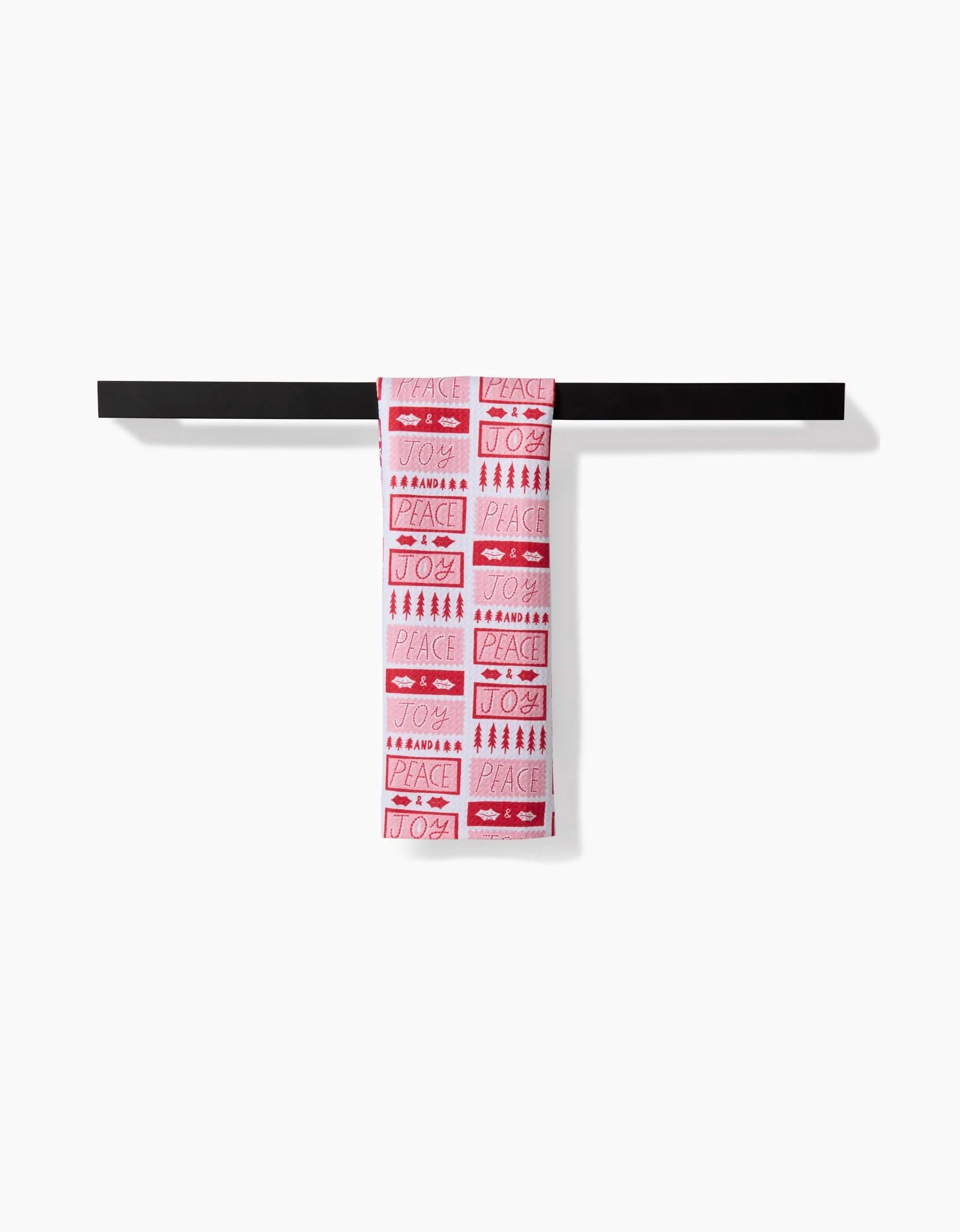 The Roxy Marj Peace Joy Stamps towel, featuring ultra-absorbent white and red fabric with holiday-themed designs and words like PEACE and JOY, hangs over a black bar against a plain white background.