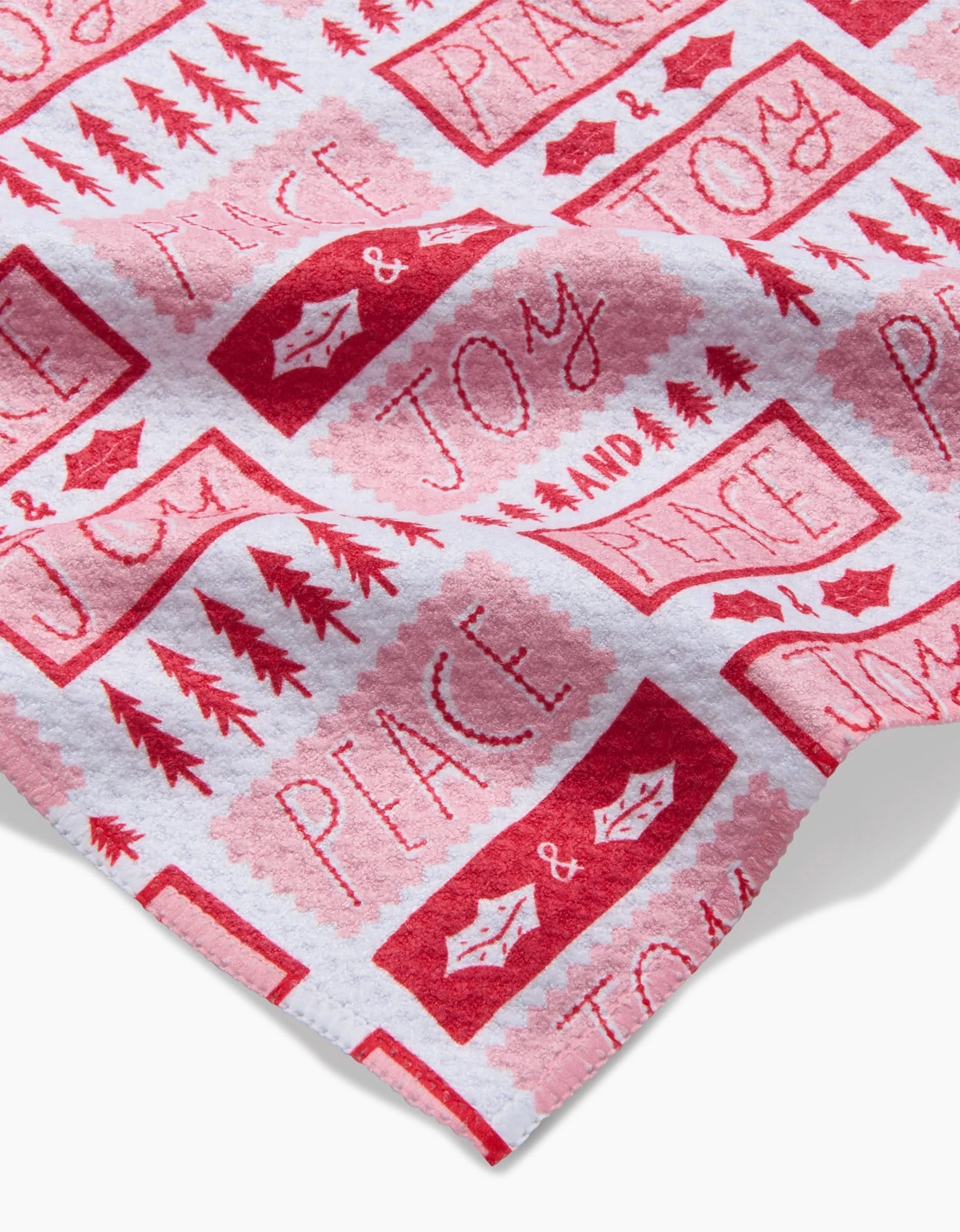 The Roxy Marj Peace Joy Stamps bar towel features red and pink “Peace & Joy” designs with trees, stars, and holly on white fabric, made from recycled materials for an eco-friendly accent.