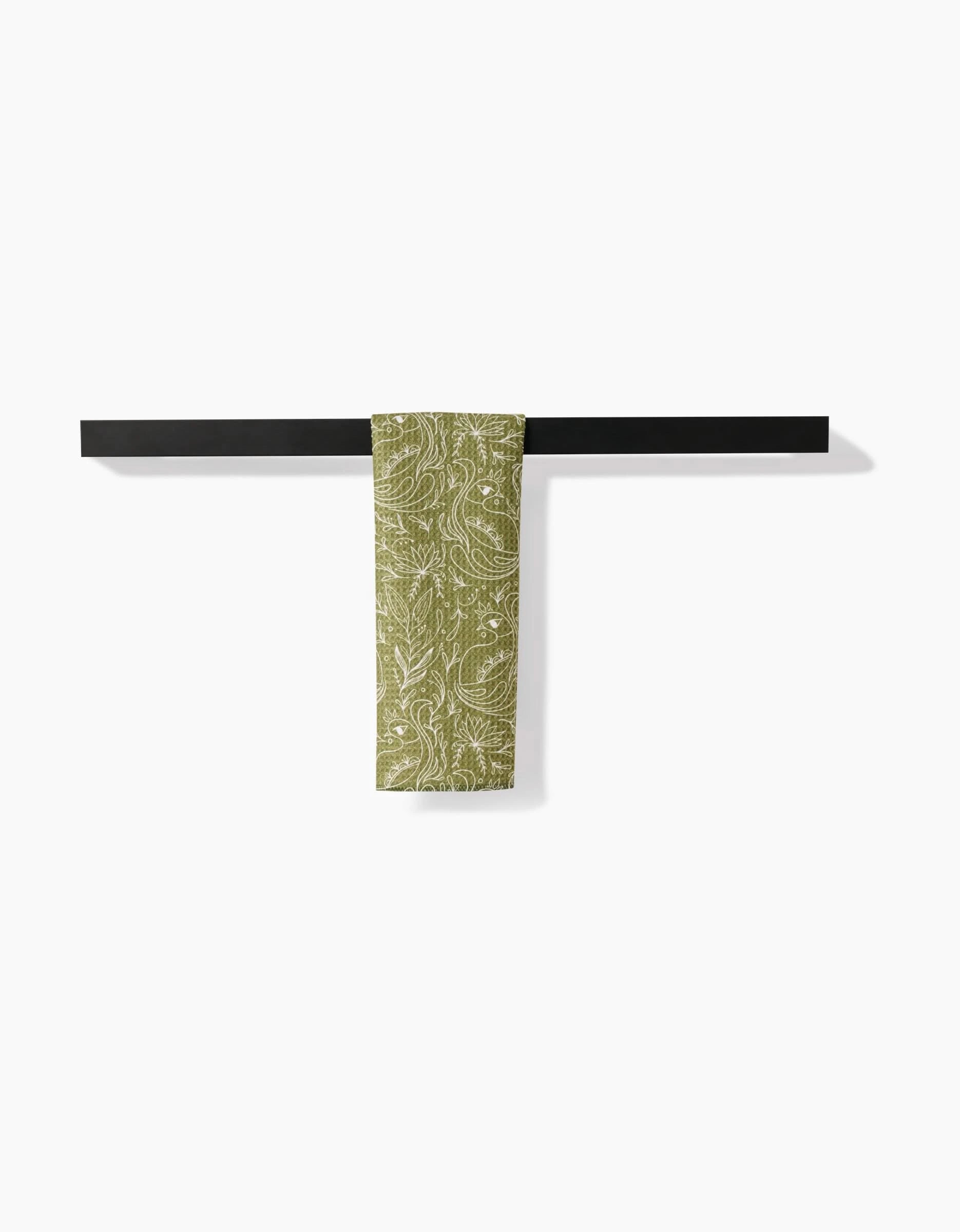 The Peacock Blooms Bar Towel by Amita Nair, made from Geoweave fabric and featuring green and white patterns, is neatly folded over a black bar against a plain white background.