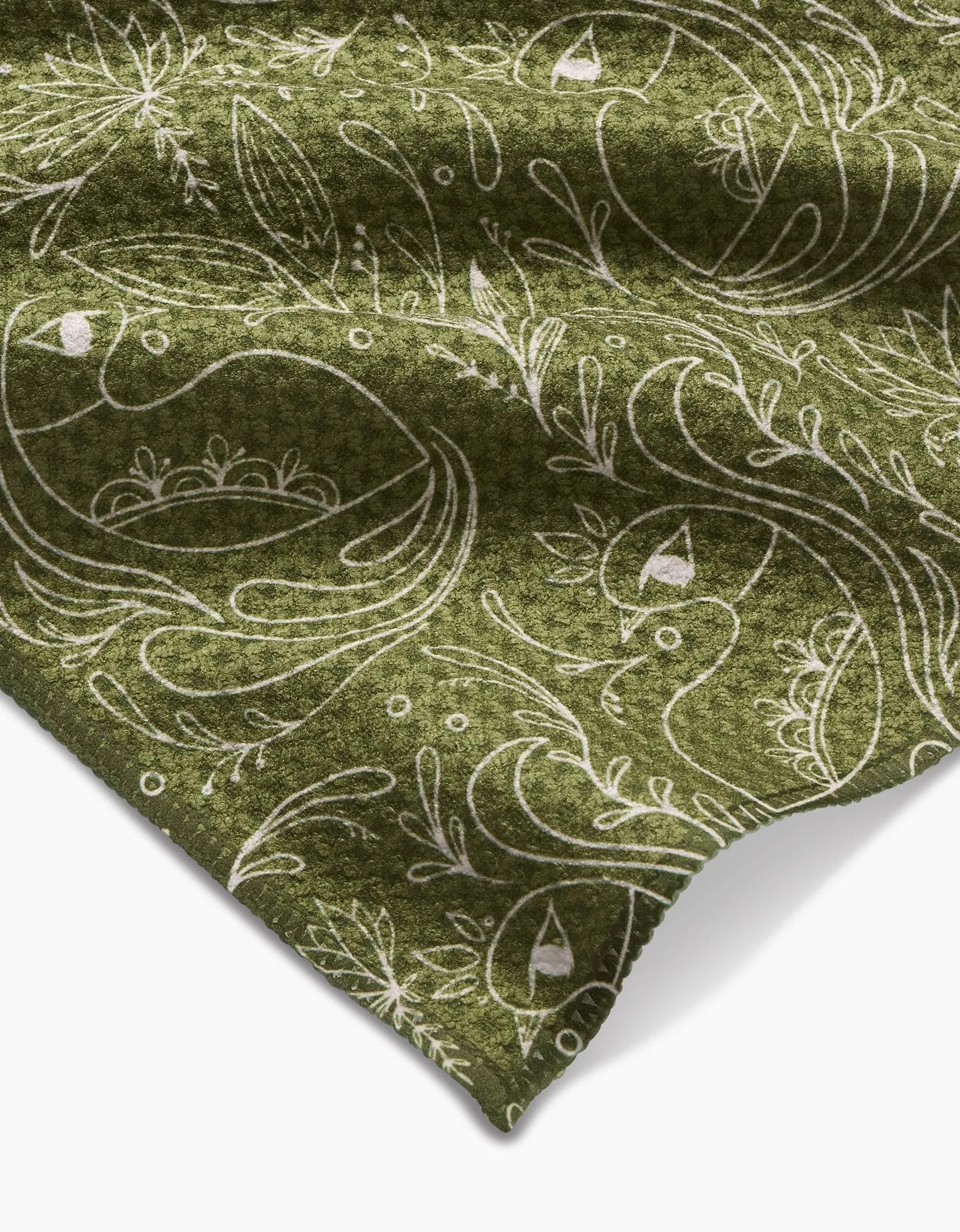 The Peacock Blooms Bar Towel by Amita Nair features green Geoweave fabric adorned with a white, whimsical bird and floral pattern. A folded corner showcases its soft texture and intricate design of stylized birds, leaves, and branches.