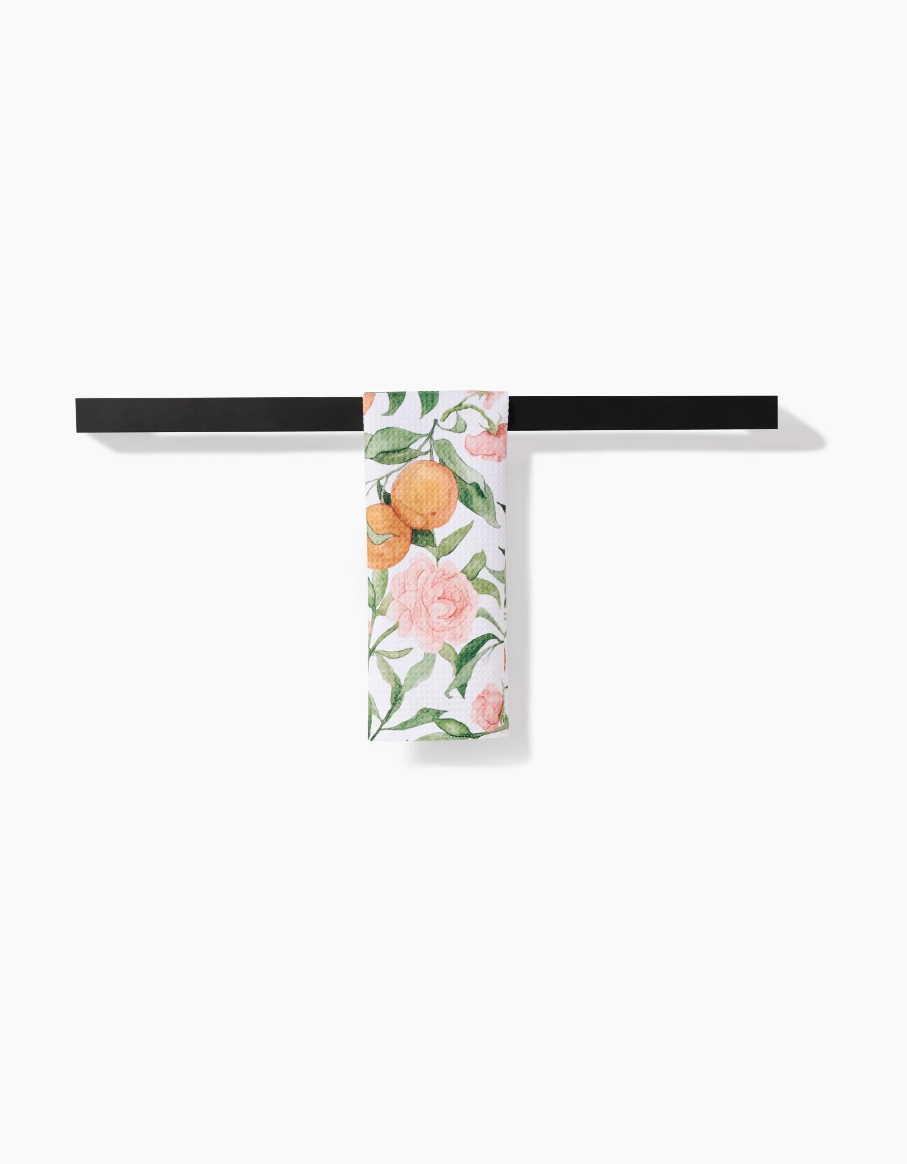 The Peony For Your Thoughts bar towel by Aubrey Fairchild, featuring pink flowers and orange fruits on ultra-absorbent Geoweave fabric, hangs neatly over a black towel bar against a white background.