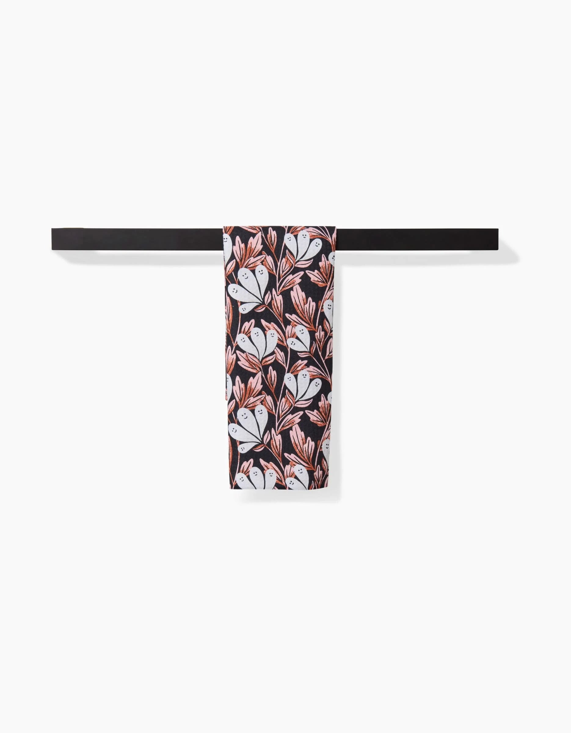 The Sarah Daugherty Phantom Floral Bar Towel, featuring white, pink, and red floral patterns on black Geoweave fabric, is showcased folded on a black towel holder against a plain white background.