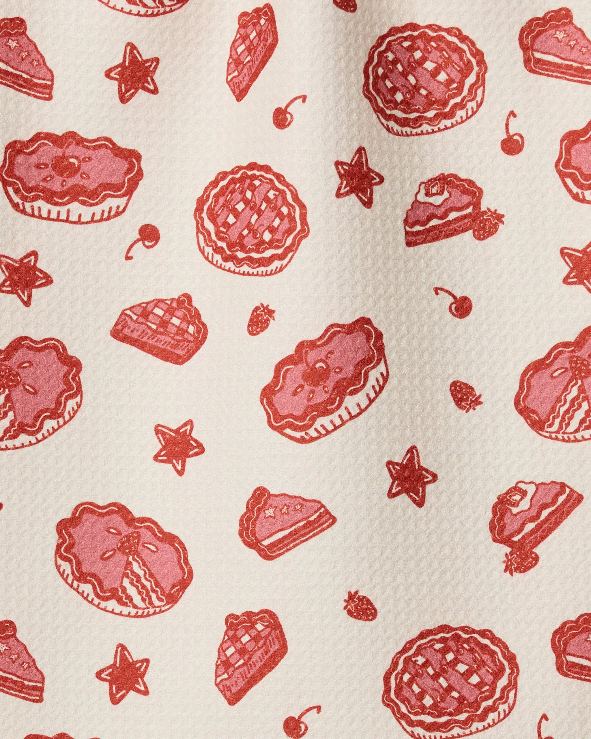 Pie-triotic by Geometry features a repeating pattern of red pies, slices, cherries, strawberries, and stars on a textured cream background—an ultra-absorbent towel that brings brightness to any kitchen.