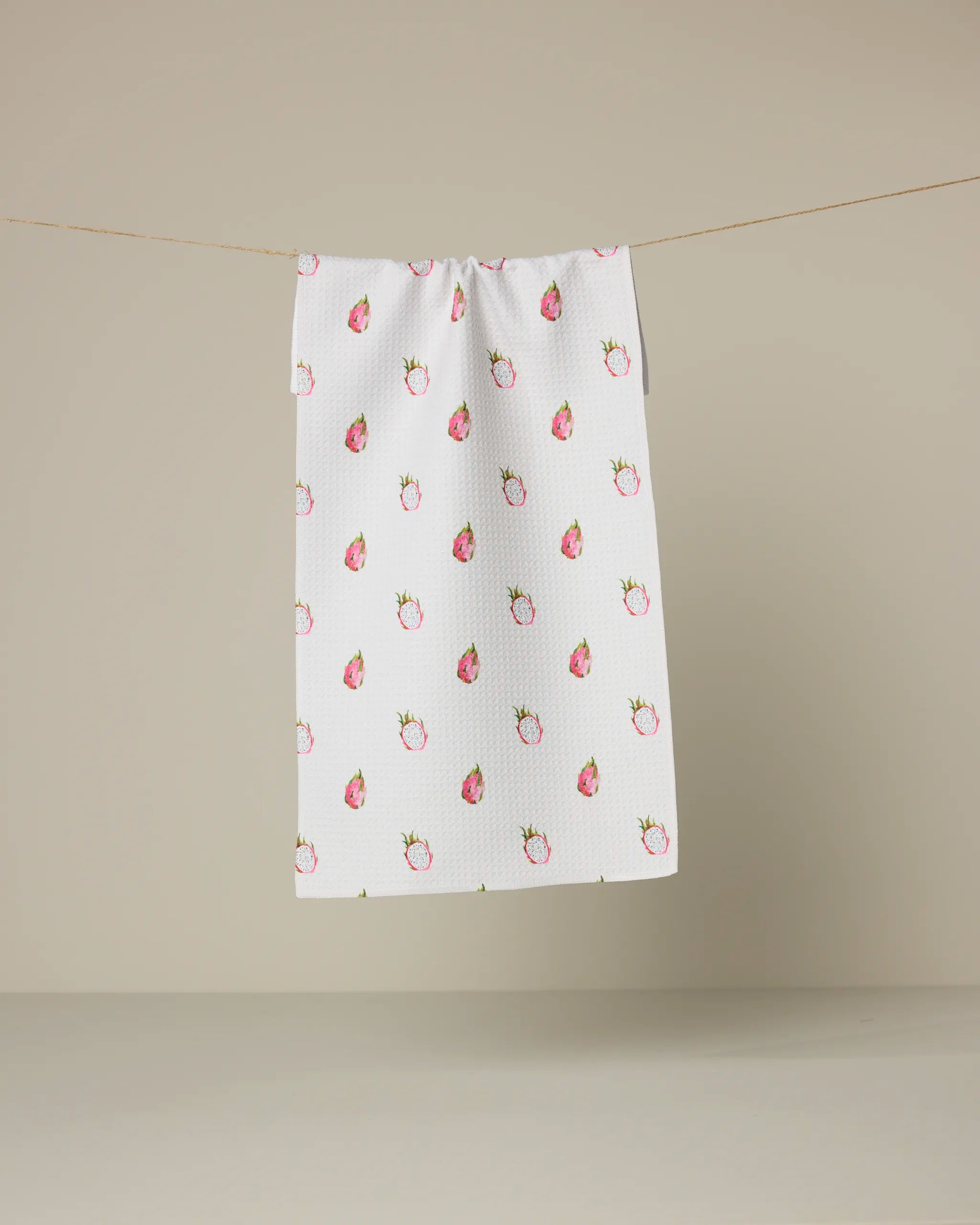 The Geometry "Pink Dragon Scattered" ultra-absorbent towel hangs on a clothesline, showcasing its pink dragon pattern against a plain beige background.