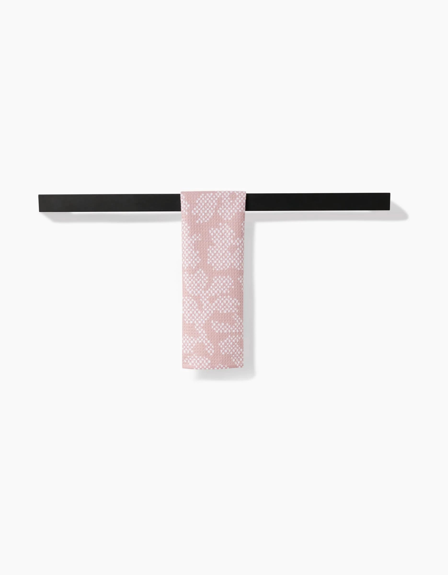 The Pixie bar towel by Studio Jeannot, featuring a pink and white pattern and made from recycled materials, is elegantly draped over a sleek black bar against a plain white background.