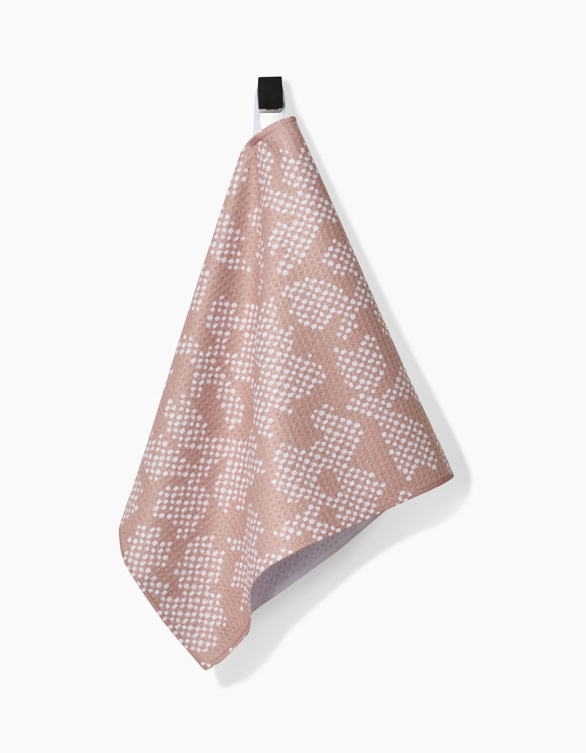 The Studio Jeannot Pixie Bar Towel, featuring a pink and white pattern and crafted from Geoweave fabric, hangs by a black loop against a plain white background.