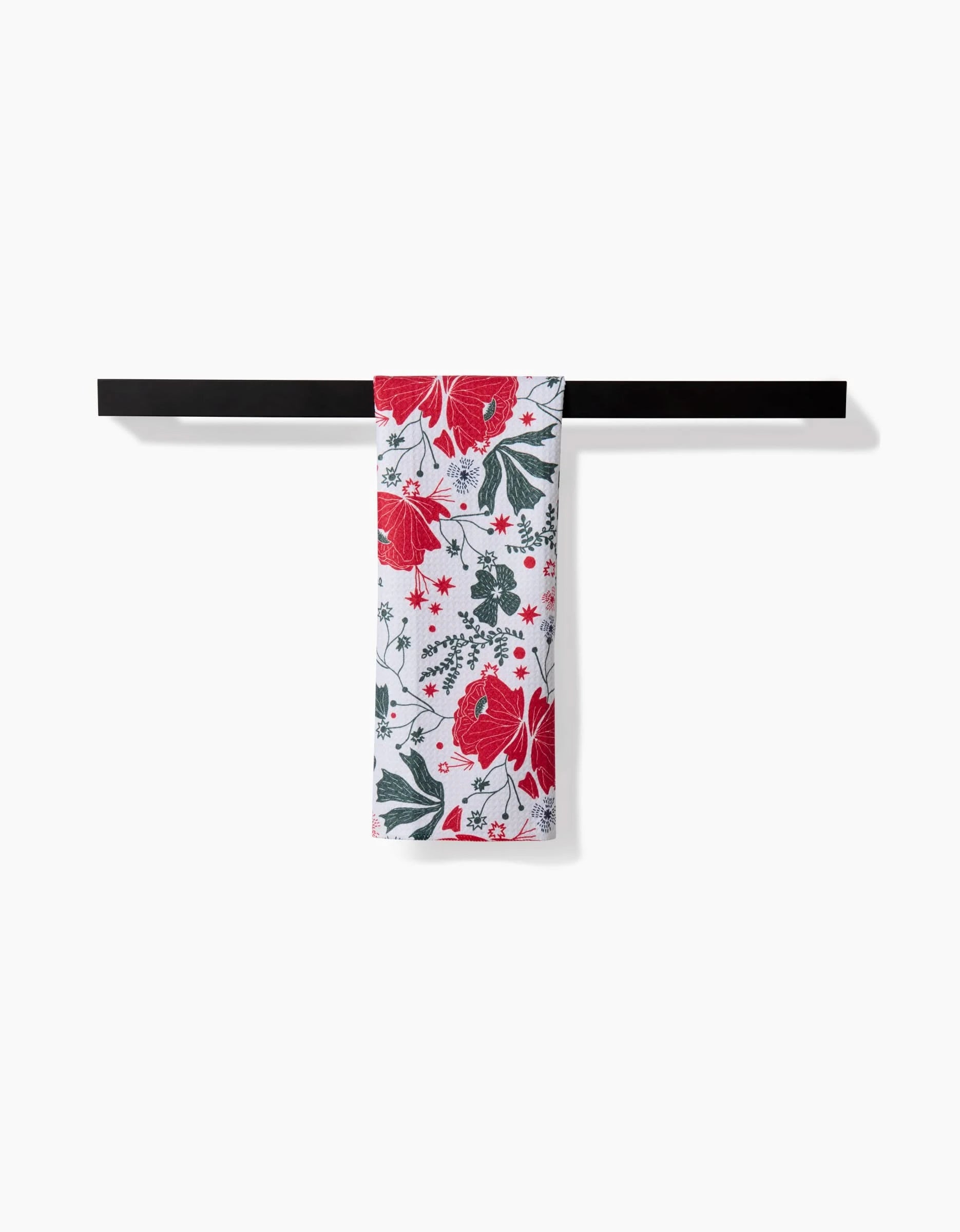 The Ash Cascade Poinsettia Bramble towel, featuring a red and green floral pattern on ultra-absorbent white fabric, is neatly folded over a black bar against a white background.