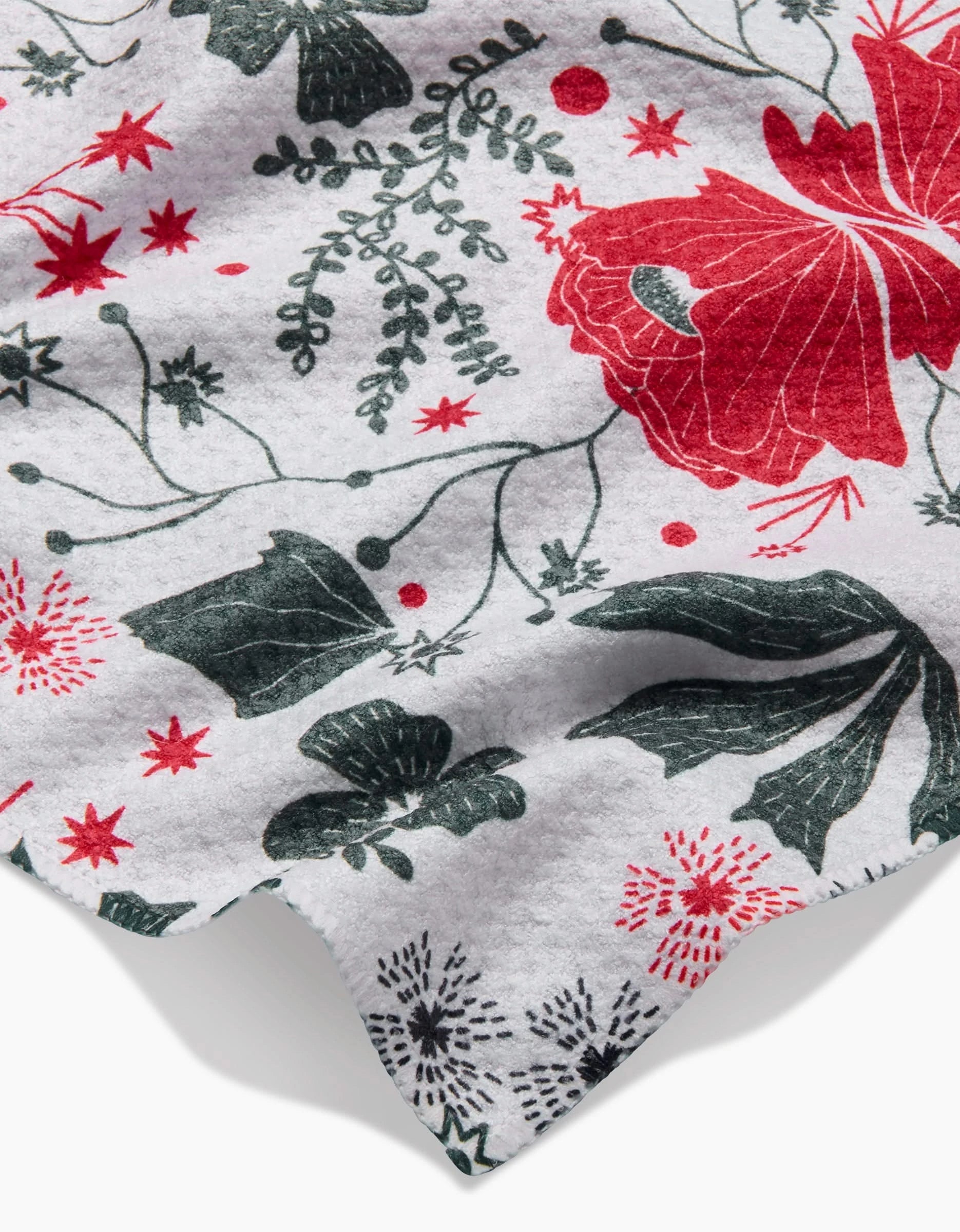 A close-up of the Ash Cascade Poinsettia Bramble towel shows its white fabric with large red poinsettias, green leaves, and small berry motifs. This ultra-absorbent towel appears slightly wrinkled.