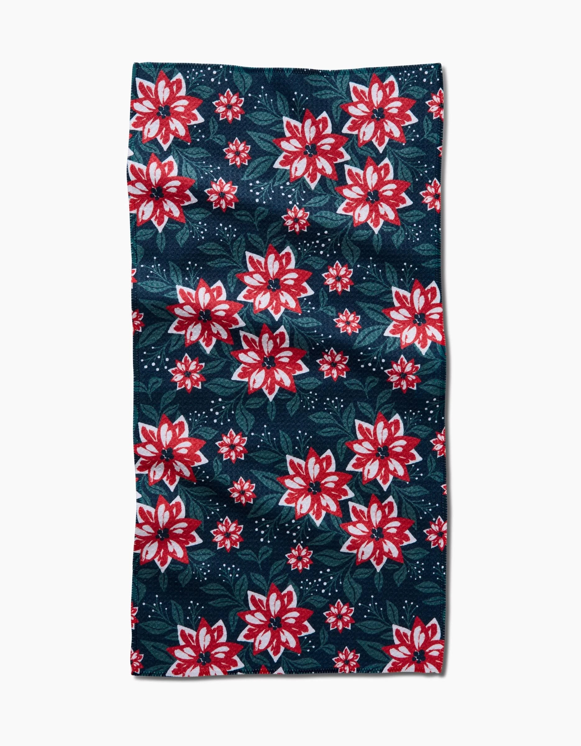 The Poinsettia Garden Bar Towel by Charlie Rowan Designs features red and white flowers with green leaves on a dark blue background with small white dots, all on Geoweave fabric. The towel has a slightly wrinkled appearance.