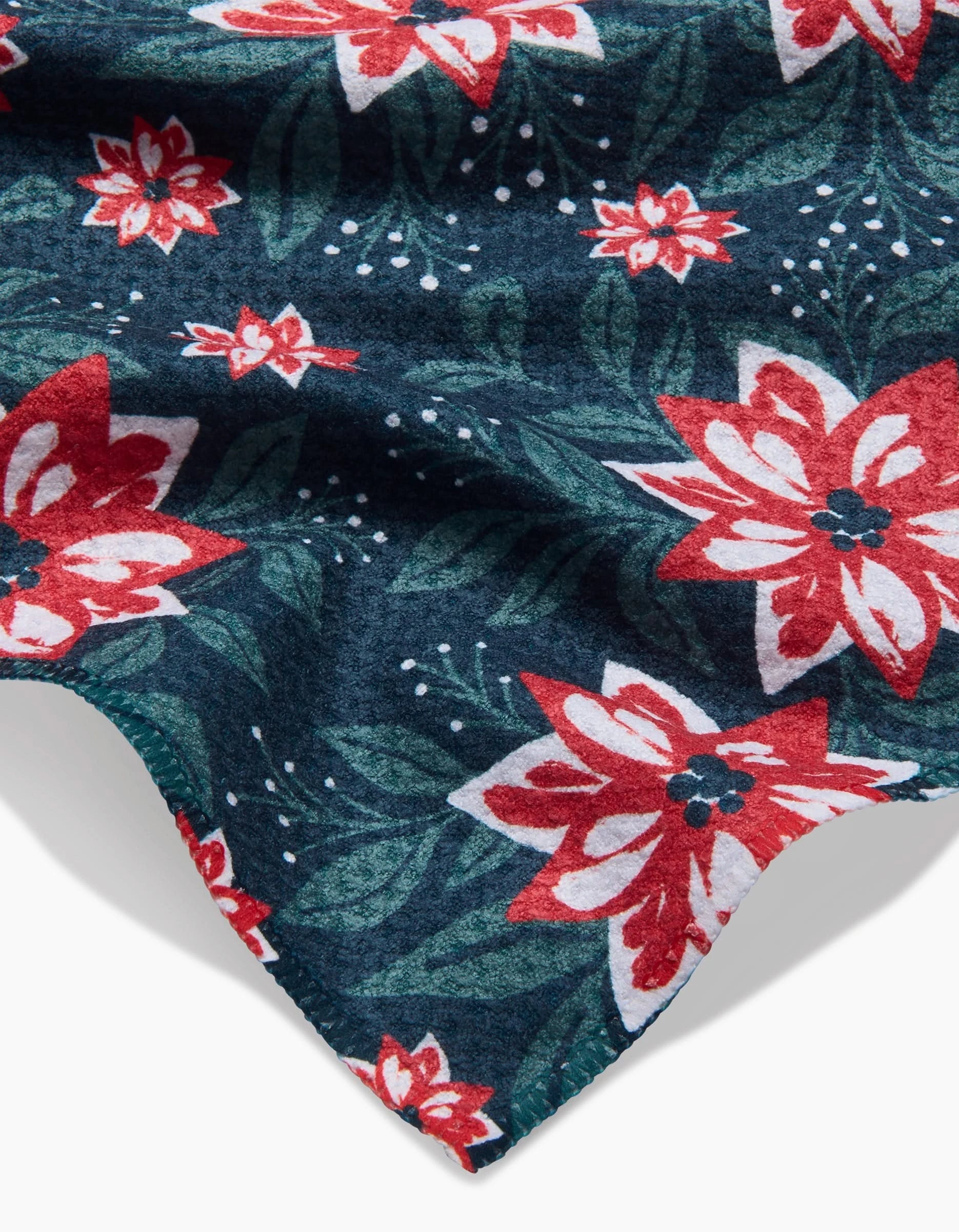 The Poinsettia Garden bar towel by Charlie Rowan Designs features a dark Geoweave fabric with vibrant red and white poinsettias, green leaves, and small white dots—a bold, textured accent to brighten any space.