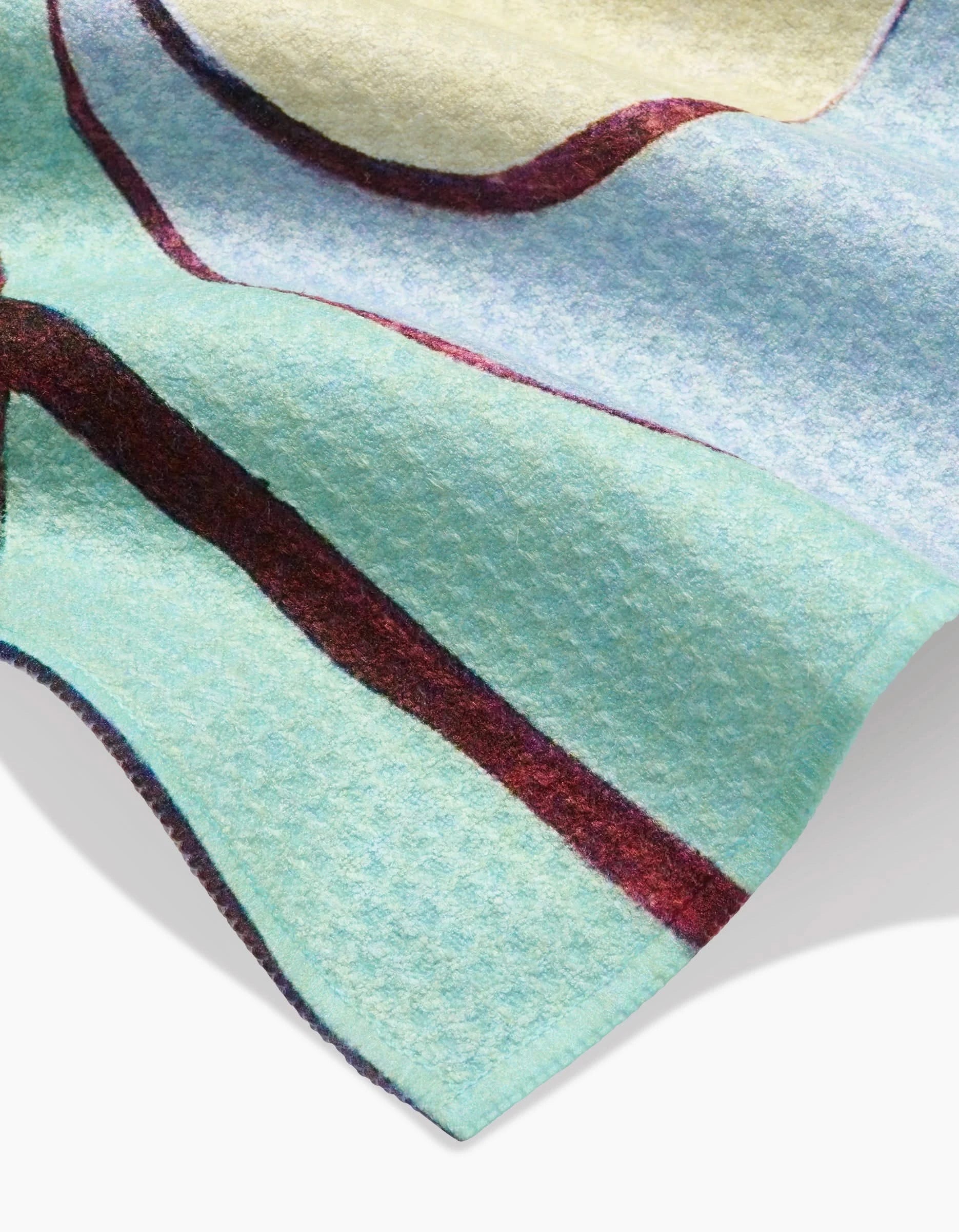 A close-up of Rachel Austin’s Poppies on Mint bar towel, made from soft recycled Geoweave fabric. The design features light blue, pale yellow, and mint green sections with wavy red and purple lines.