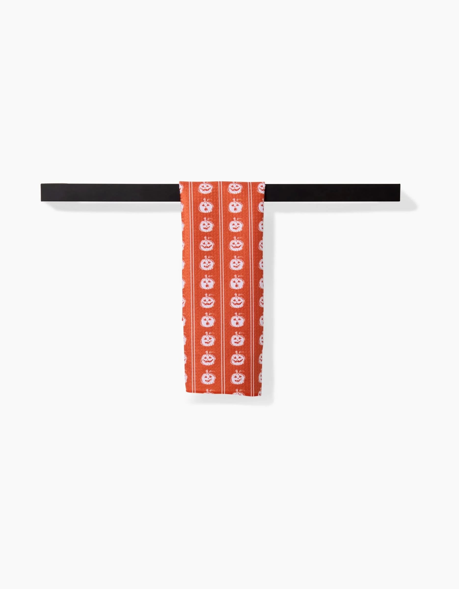 The Aubrey Fairchild Pumpkin Pinstripes towel, ultra-absorbent and featuring a red design with white floral patterns, hangs neatly folded over a black bar on a plain white background.