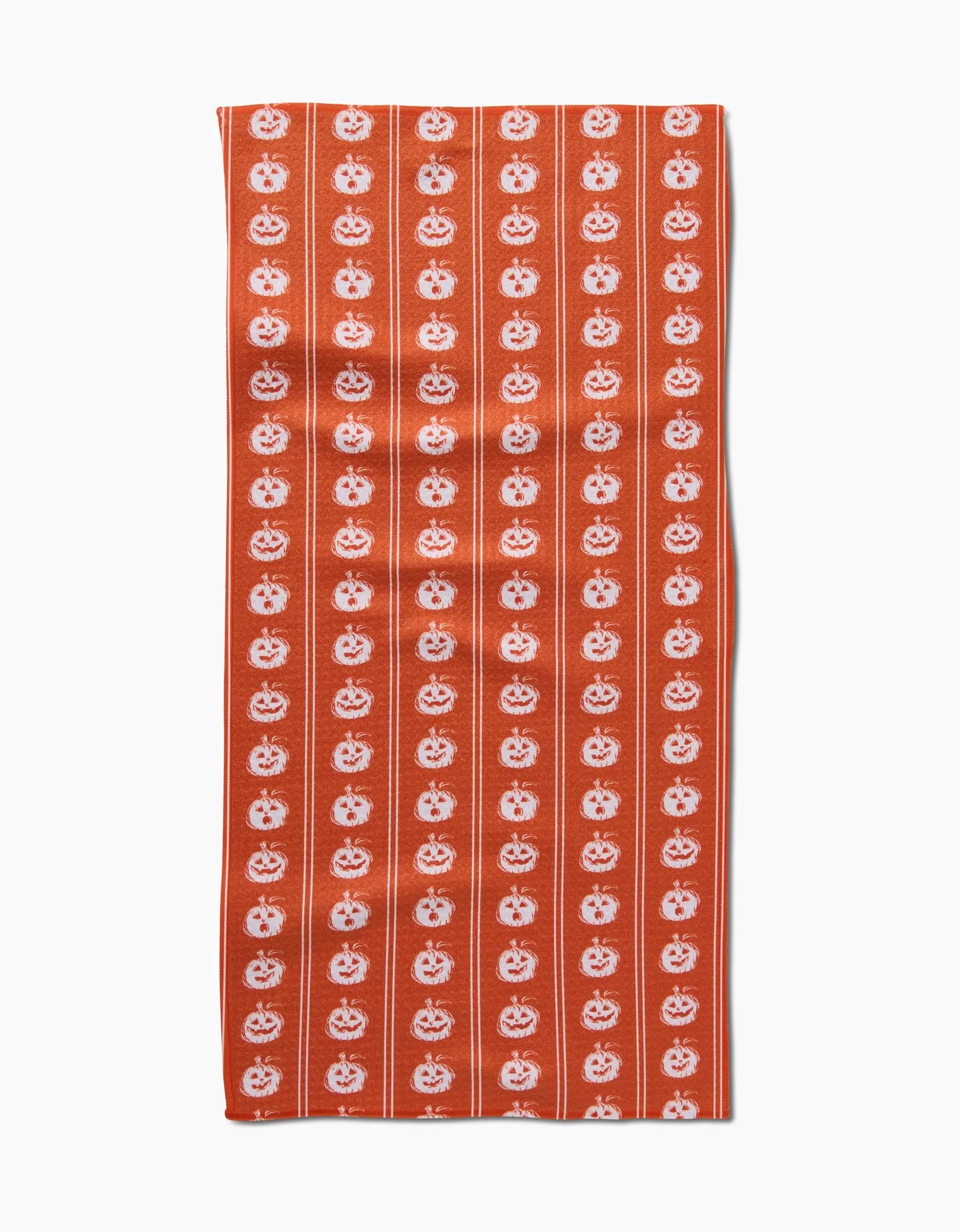 The Aubrey Fairchild Pumpkin Pinstripes towel is ultra-absorbent and features evenly spaced vertical rows of white jack-o-lantern faces on a vibrant orange background.