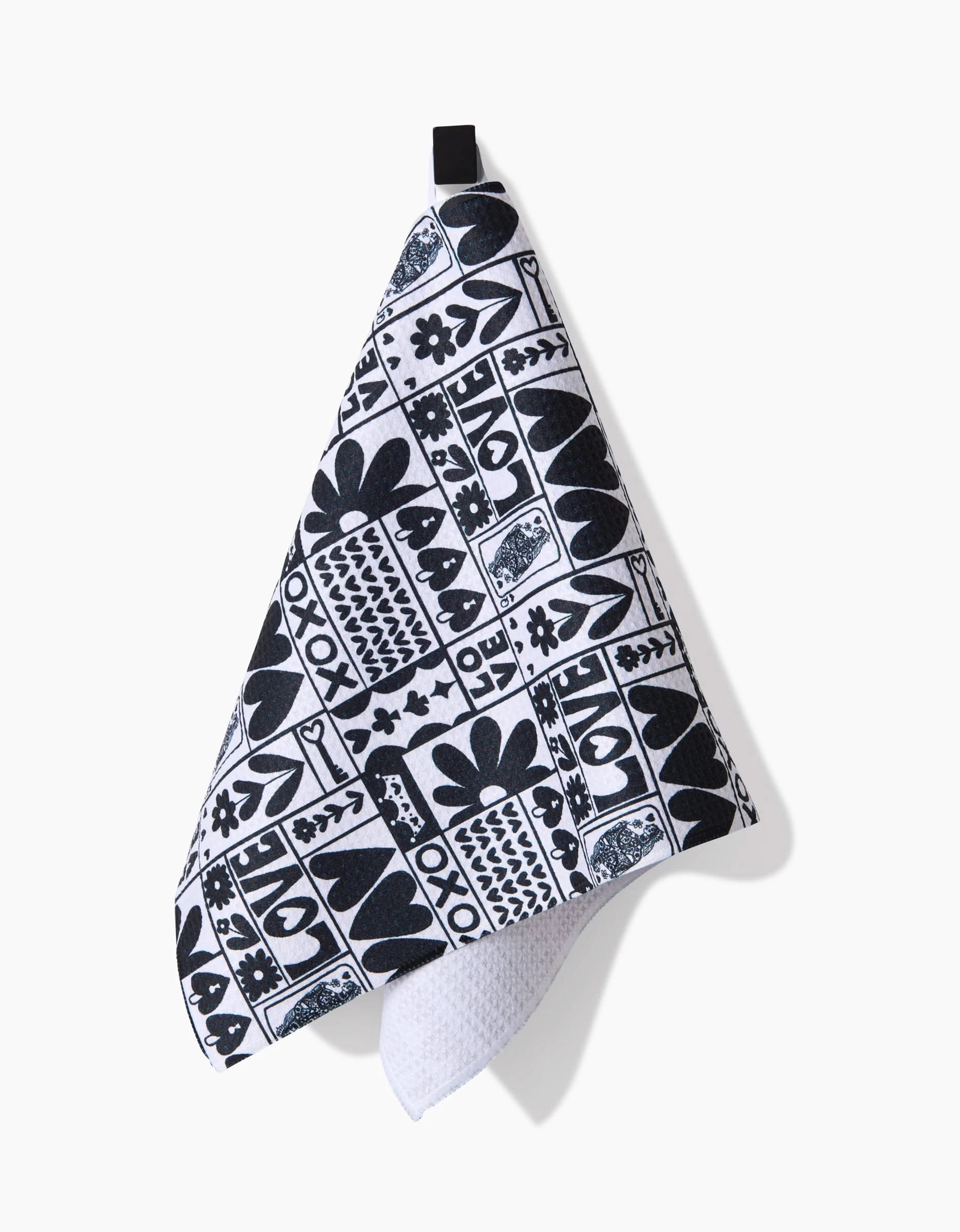 The Queen of Hearts bar towel by Kayla Ann features black and white geometric and floral patterns. It hangs from a black loop, showcasing its textured, ultra-absorbent underside—ideal for any kitchen or bar.