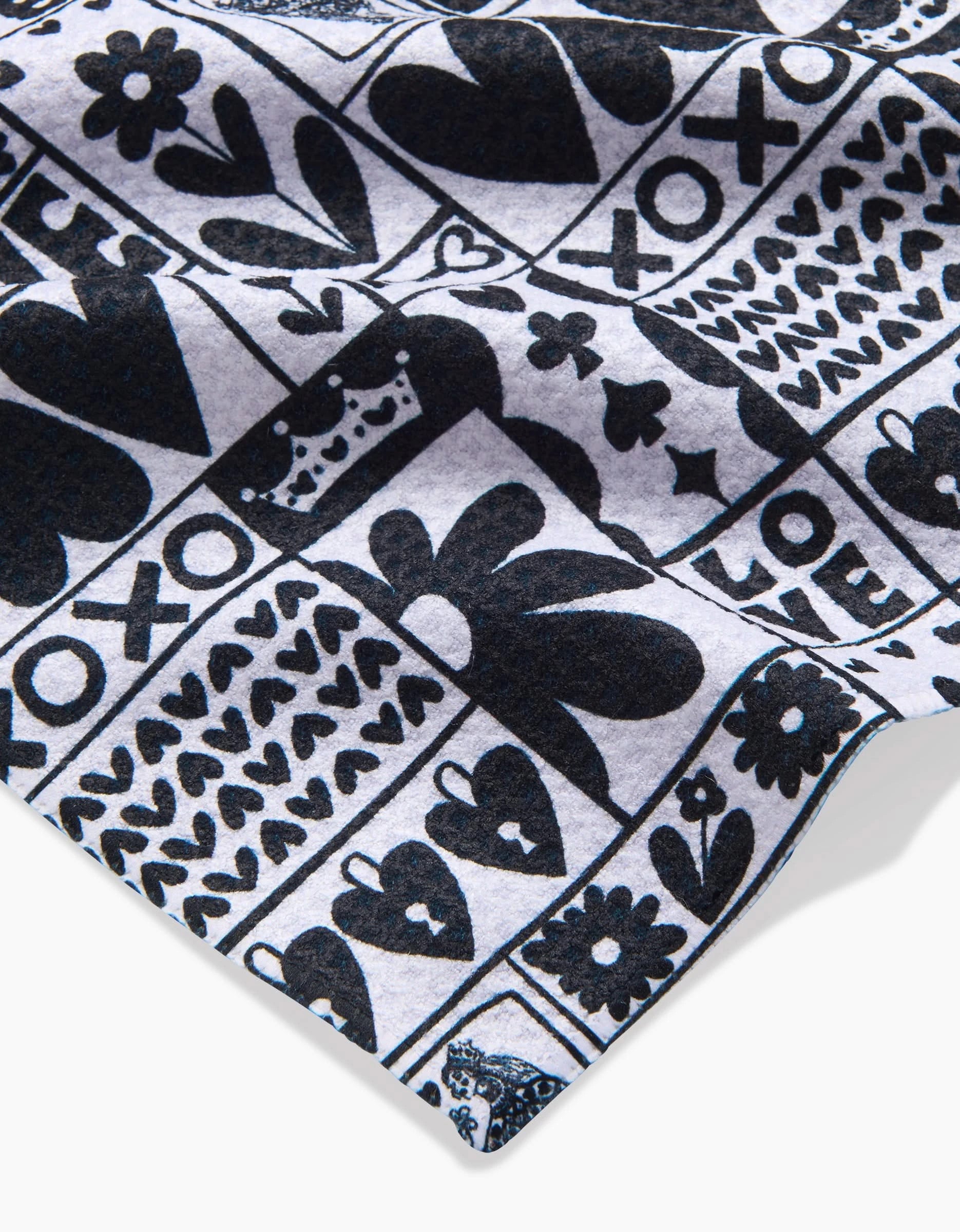 Close-up of the Kayla Ann Queen of Hearts bar towel, made from recycled materials with a black and white grid pattern featuring hearts, flowers, crowns, XOXO, and more. The ultra-absorbent fabric appears slightly wrinkled.