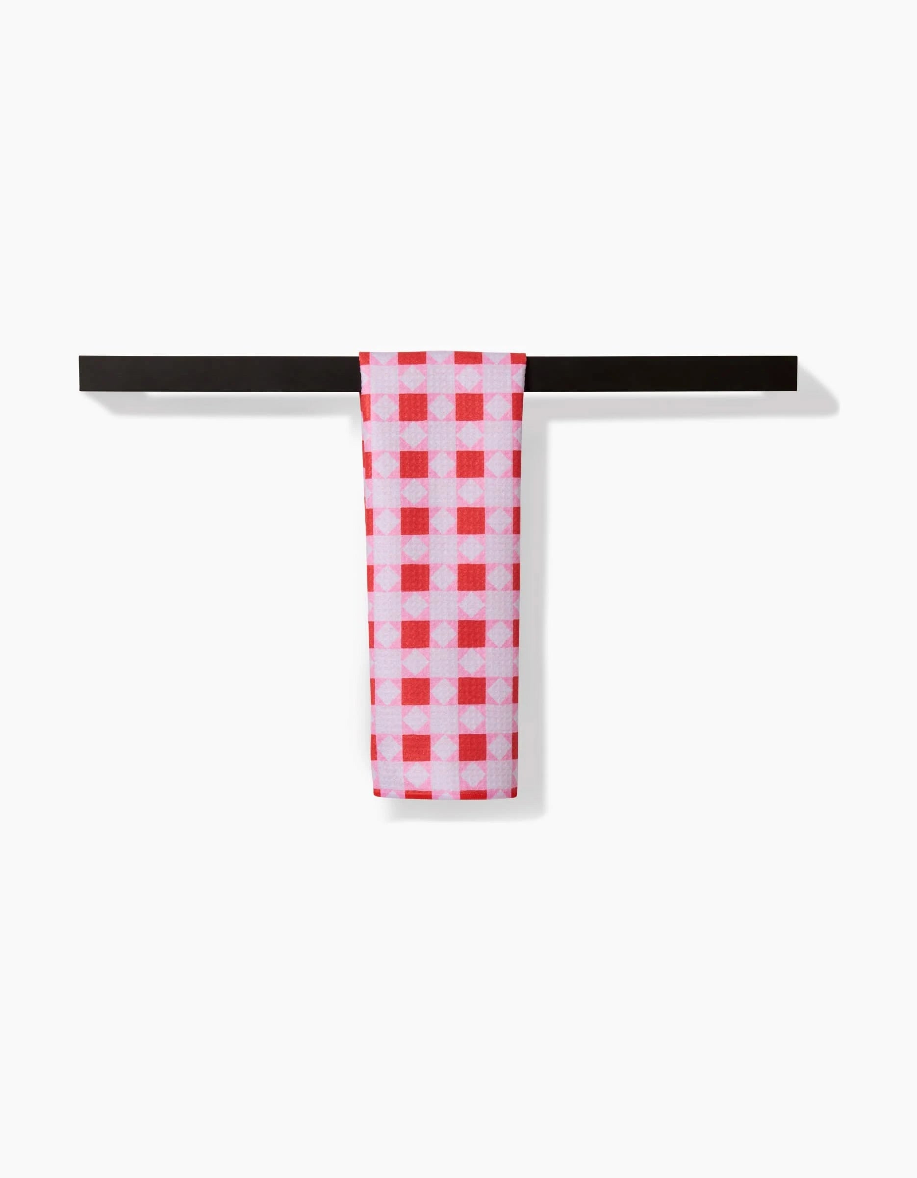 The Quilt Block Pink Andred bar towel by Brittany Jepsen, featuring a red and white checkered Geoweave fabric, hangs neatly over a simple black bar against a plain white background.