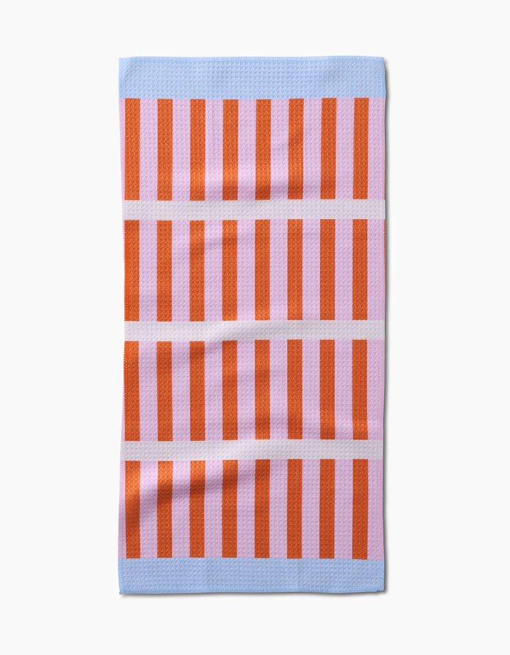 The Red Glow Bar Towel by Happy Hemera features vertical red and pink stripes with light blue bands at the top and bottom, separated by three pink lines. Made from Geoweave fabric, it lies flat on a white background.