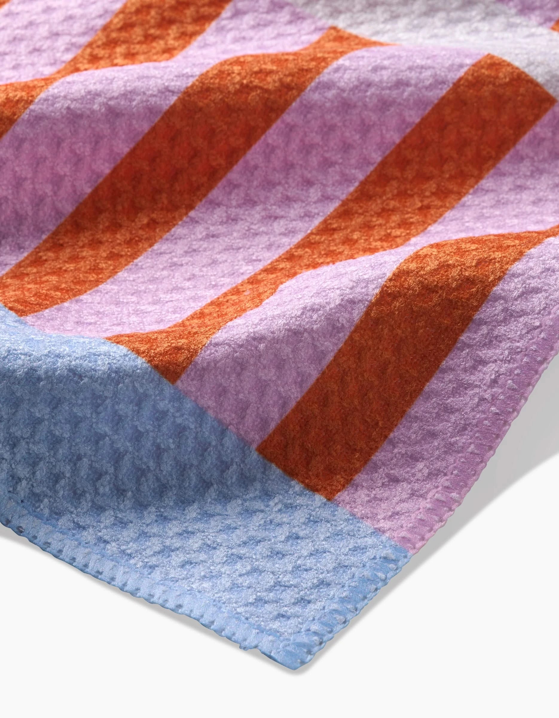 A close-up of Happy Hemera’s Red Glow Bar Towel, crafted from Geoweave fabric with wide purple and orange stripes, a pale blue border, and a soft, wavy waffle-like texture.
