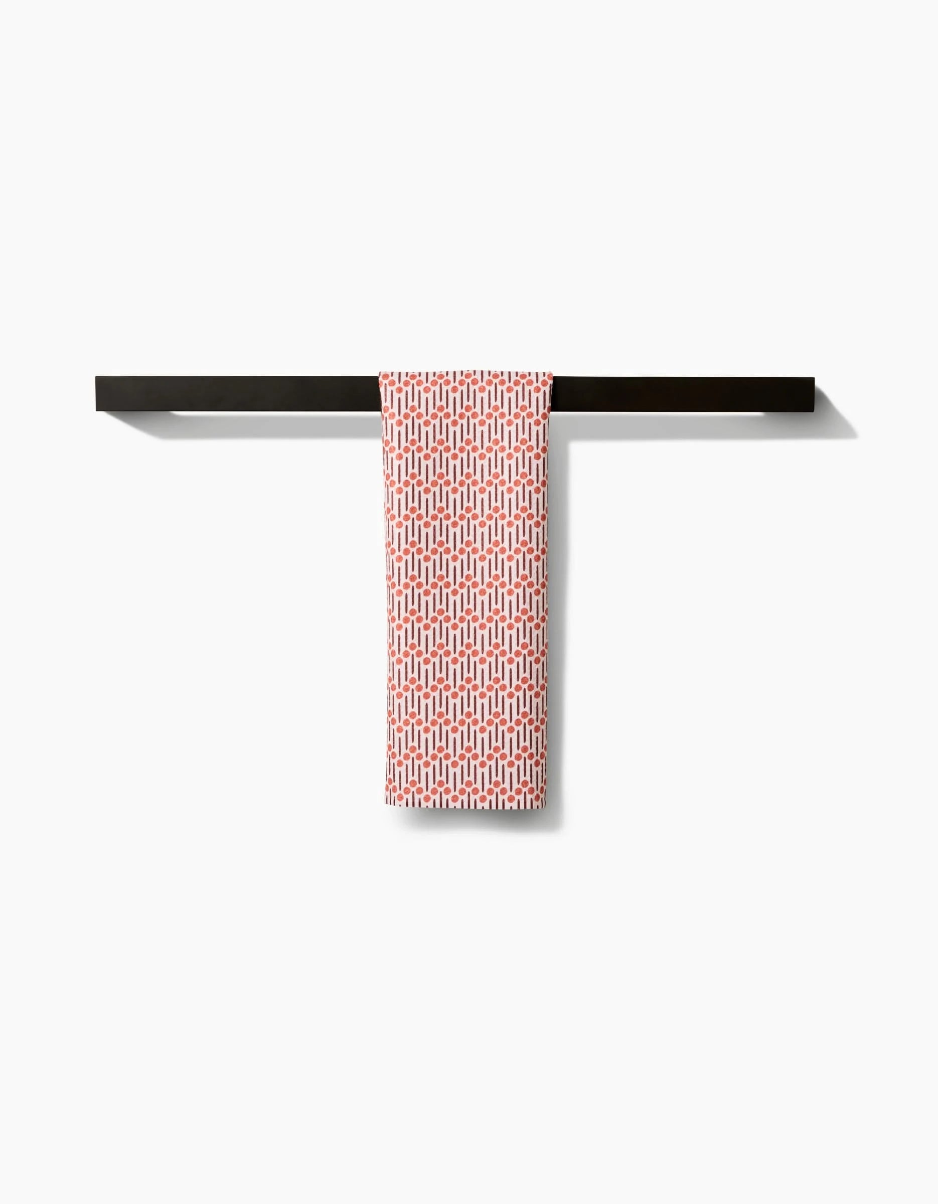 The Retro Geo Bar Towel by Teri the Butter, featuring a red and white pattern and made from recycled materials, hangs neatly over a sleek black towel bar against a plain white background.