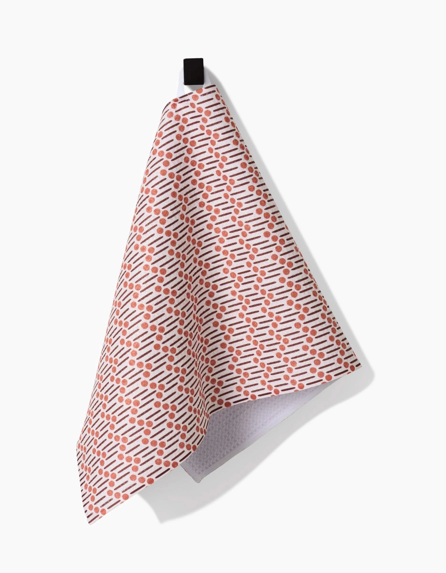 The Retro Geo bar towel by Teri the Butter, made from recycled materials and patterned with small orange dashes, hangs from a black loop against a plain white background.