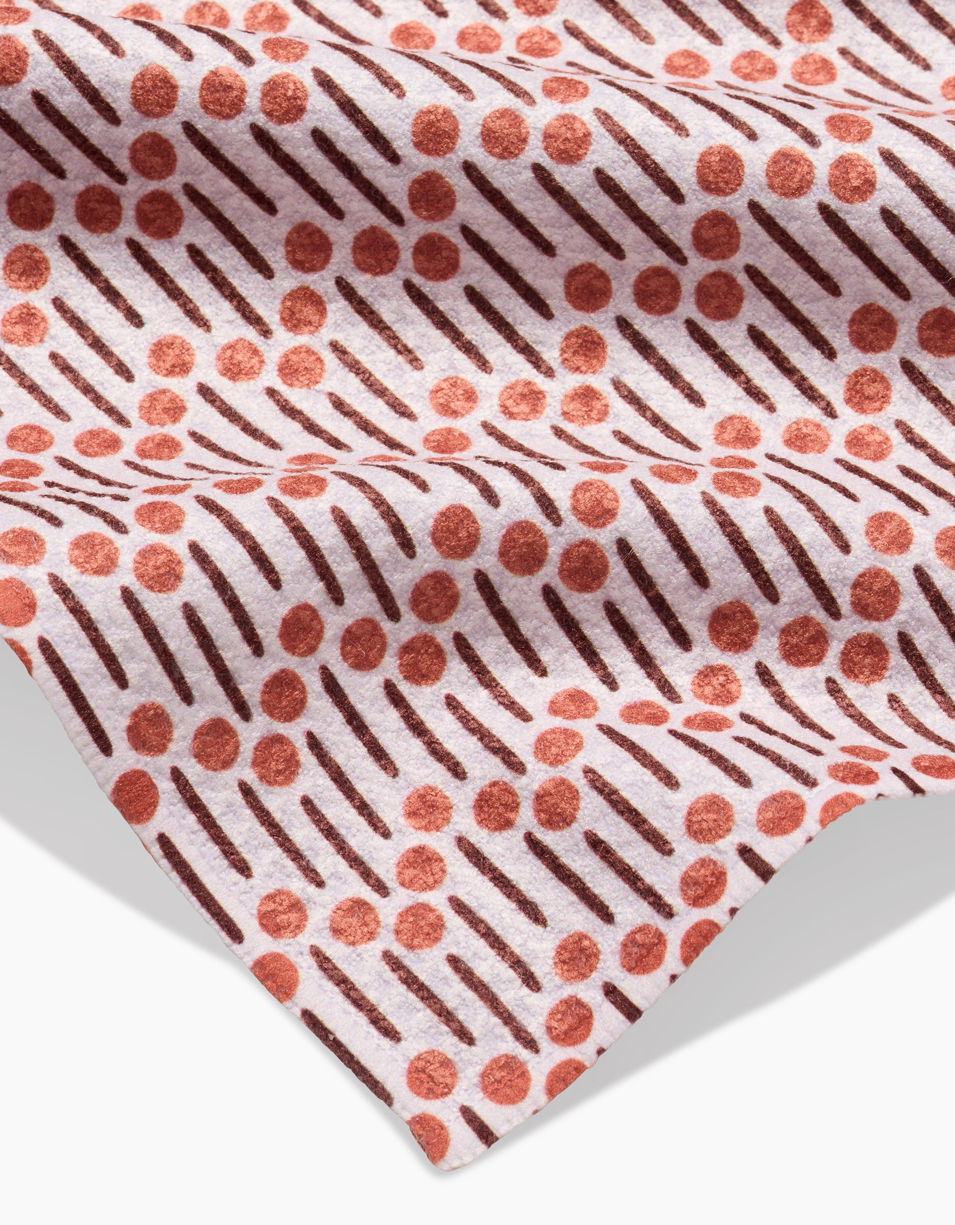 A close-up of Teri the Butter’s Retro Geo Bar Towel on a pink background displays its Geoweave fabric, crafted from recycled materials, with diagonal dark lines and scattered red dots enhanced by soft folds and shadows.