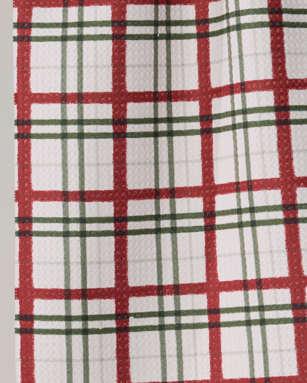 A close-up of Geometry’s Ribbon Plaid mini towel, featuring a white textured Geoweave fabric with intersecting red and green plaid lines that highlight its quality craftsmanship.