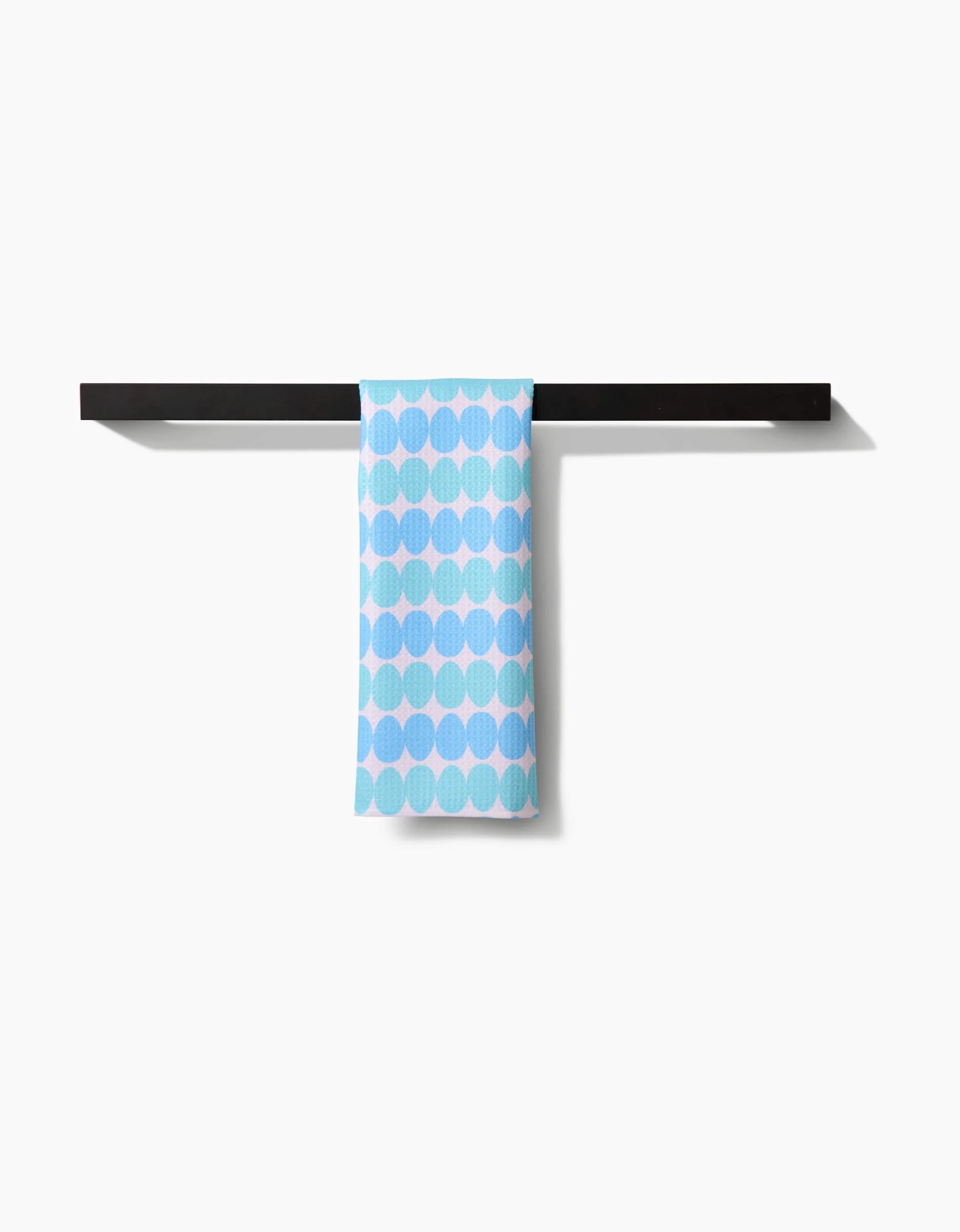 The Kayla Ann Robins Egg Bar Towel, featuring light blue dots on soft Geoweave fabric, hangs over a sleek black towel bar against a white background. It offers superior absorbency and quick drying.